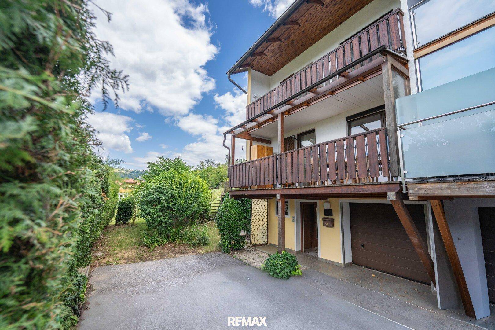Seitenansicht des Hauses mit Garage, Balkonen und gepflegter Hecke.