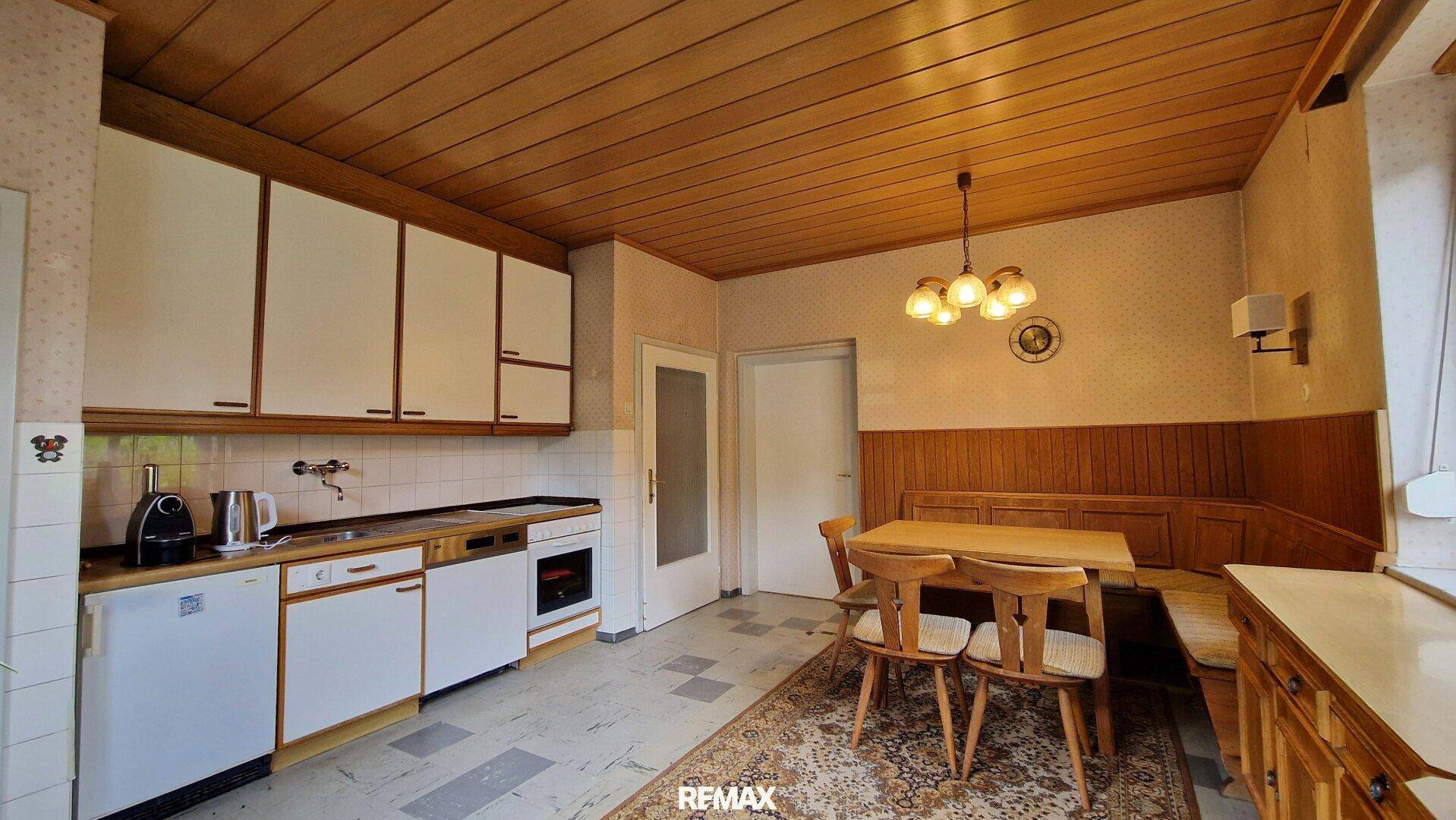 Funktionale Küche mit weißen Schränken, Holzdecke und integriertem Essbereich für die Familie.