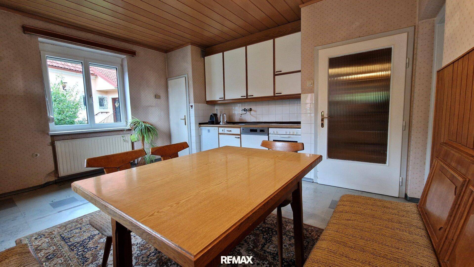 Essbereich in der Küche mit Holztisch und Blick auf die weißen Küchenschränke und Geräte.