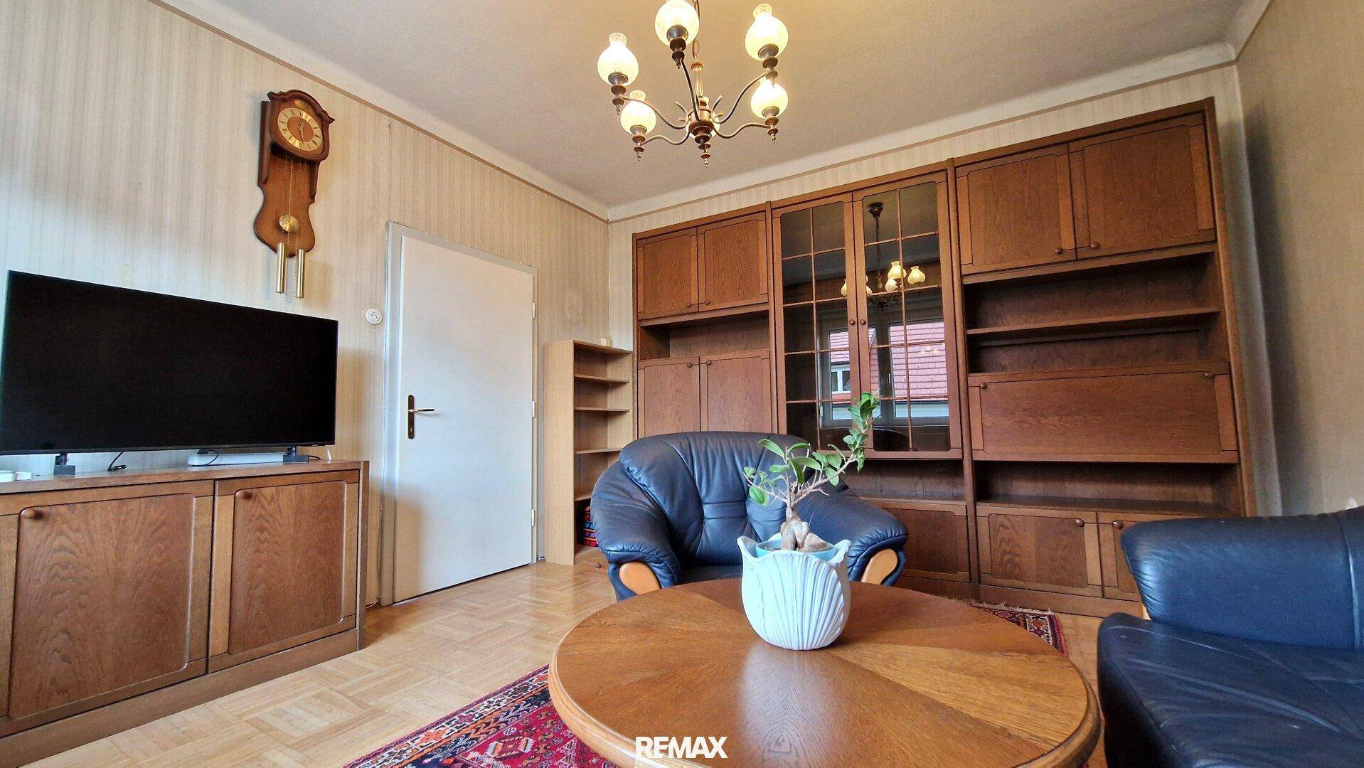 Gemütliches Wohnzimmer mit Holzschrankwand, Ledersofa und klassischem Kronleuchter als Blickfang.