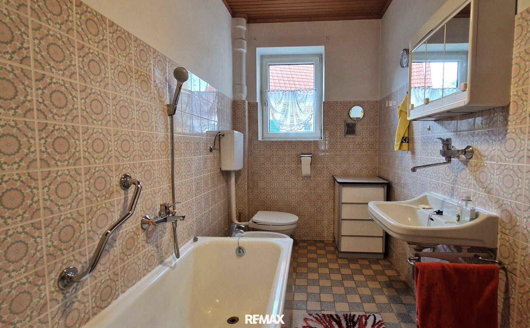 Badezimmer mit Badewanne, Waschbecken und gemusterten Fliesen im charmanten 80er-Jahre-Stil.