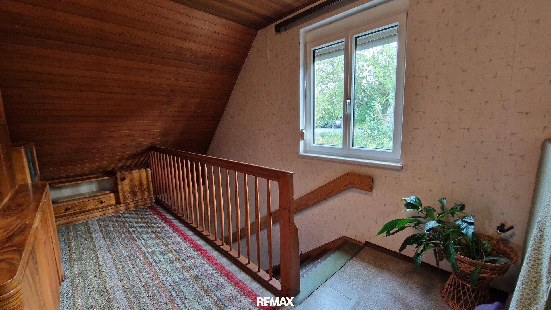 Obergeschoss-Flur mit Holzgeländer, Dachschräge und Blick aus dem Fenster ins Grüne.