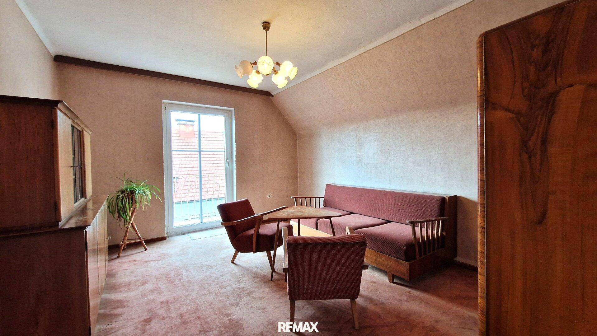 Gemütliches Wohnzimmer im Dachgeschoss mit Dachschräge und Zugang zum Balkon, sehr hell.