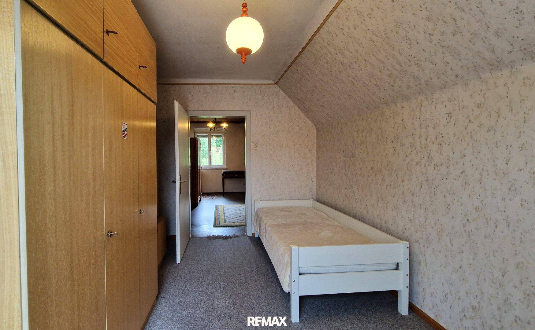 Dachgeschoss-Schlafzimmer mit Einzelbett, Schrankwand und Zugang zu einem weiteren Raum.