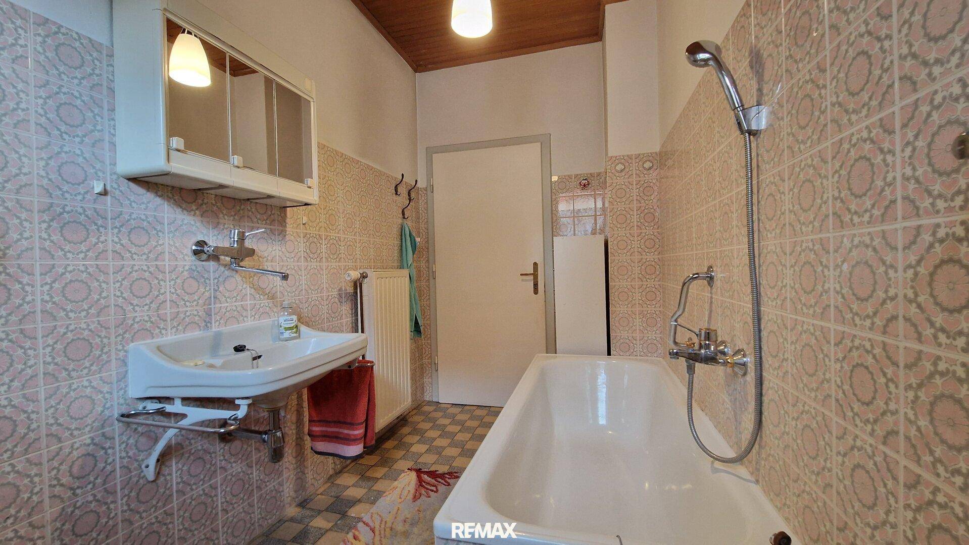 Badezimmer mit Badewanne, Waschbecken und rosa gemusterten Wandfliesen, funktional und hell.