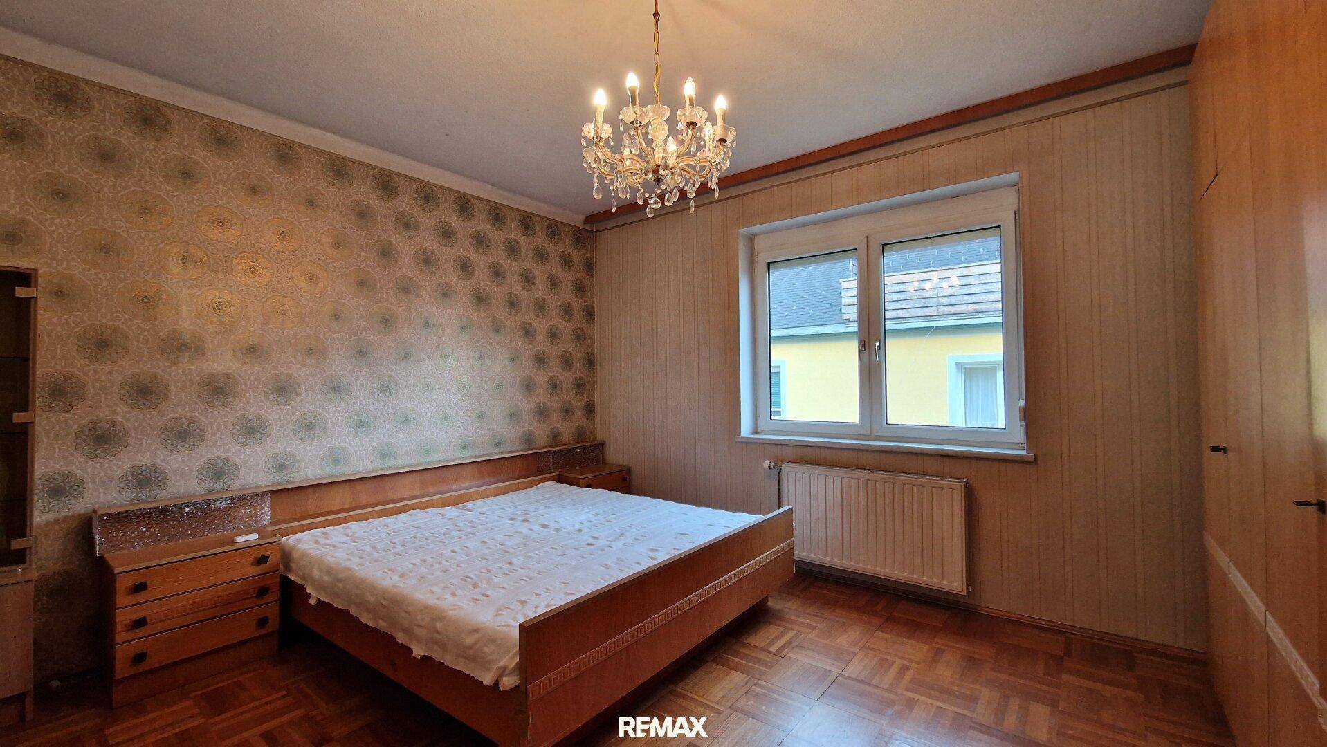 Schlafzimmer mit Parkettboden, Doppelbett und gemusterter Tapete, bietet eine ruhige Atmosphäre.
