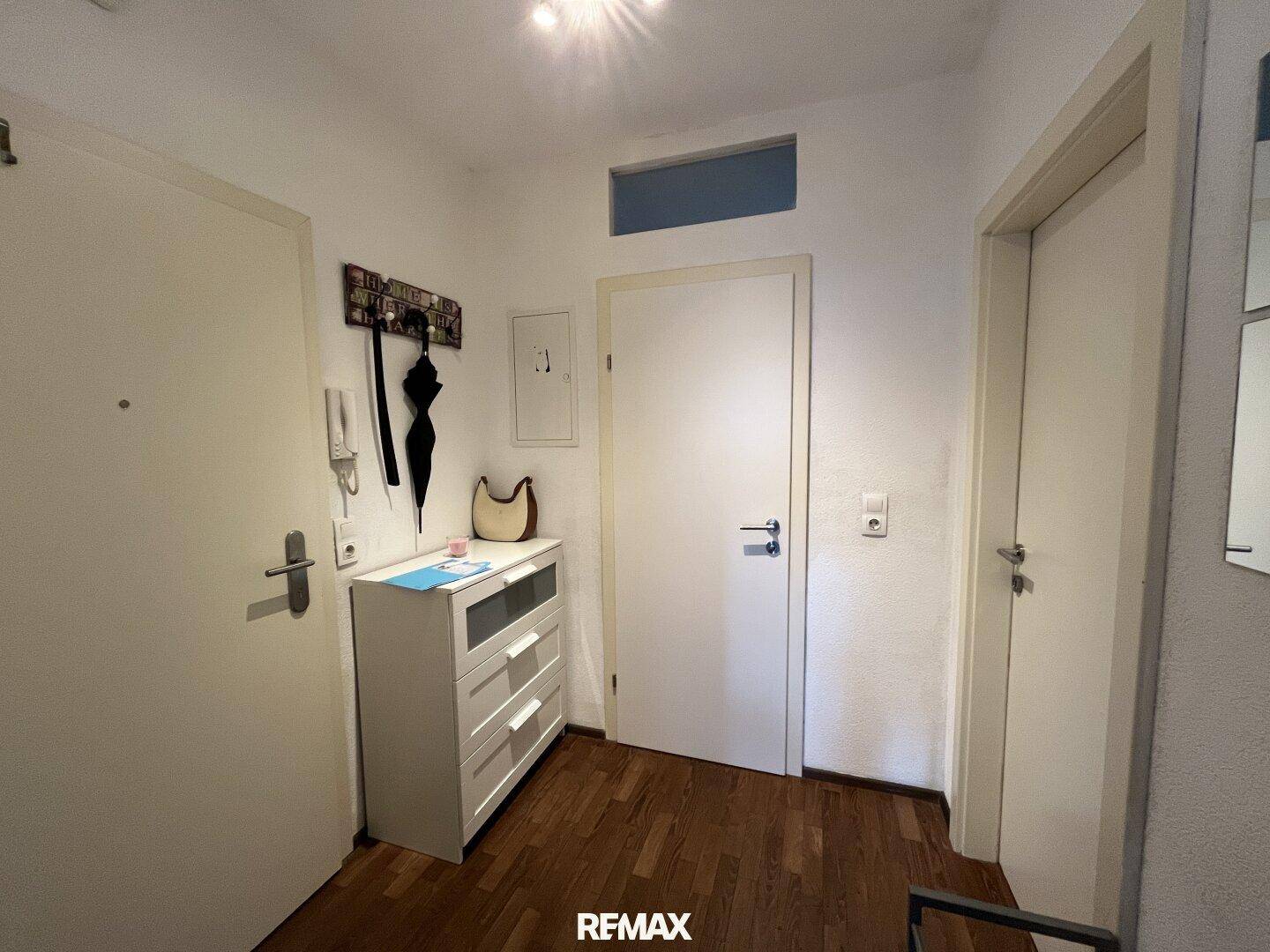 Heller Eingangsbereich mit Holzboden, weißer Kommode und Garderobe.