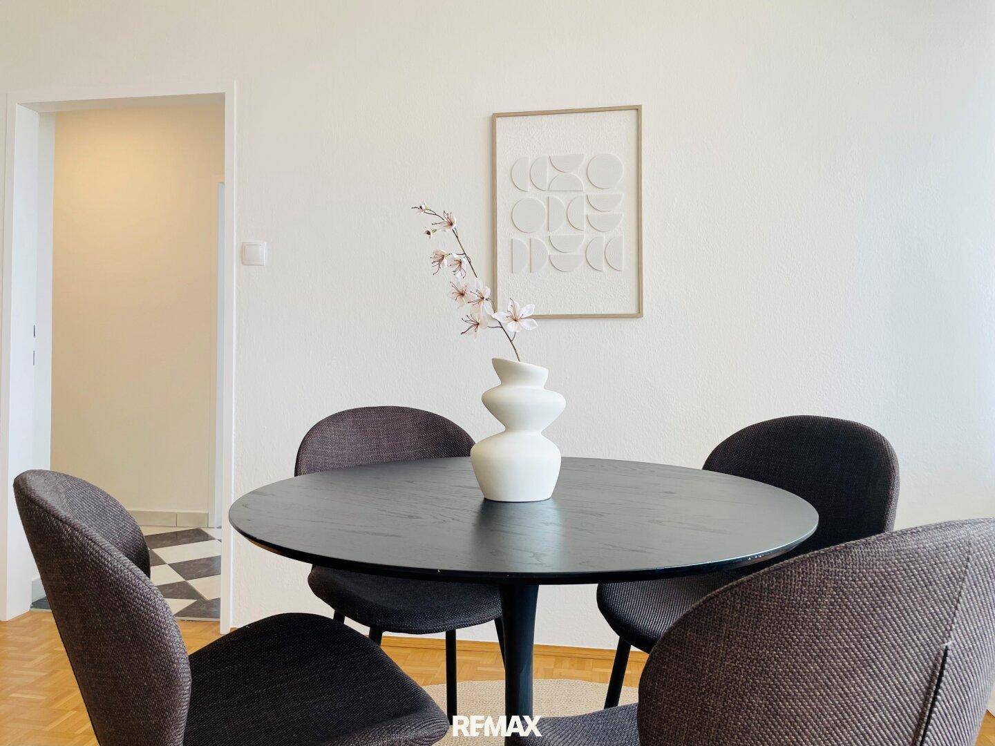Moderner Essbereich mit rundem Tisch, dunklen Stühlen und minimalistischer Wandkunst.