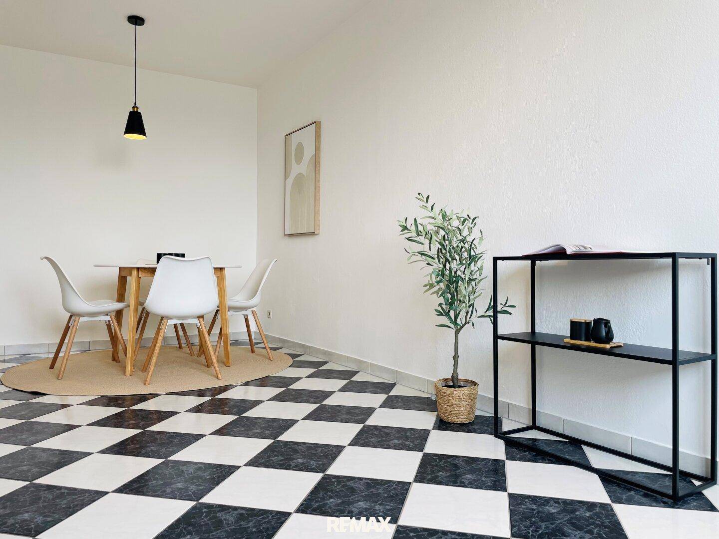 Essbereich mit schwarz-weißem Fliesenboden, Holztisch und moderner Dekoration.