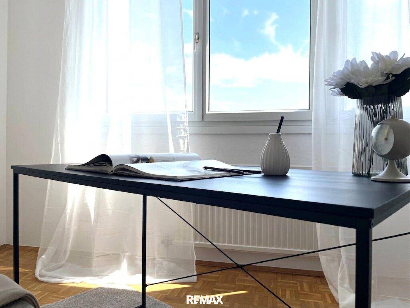 Heller Arbeitsbereich mit Schreibtisch, Fenster und transparenten Vorhängen.