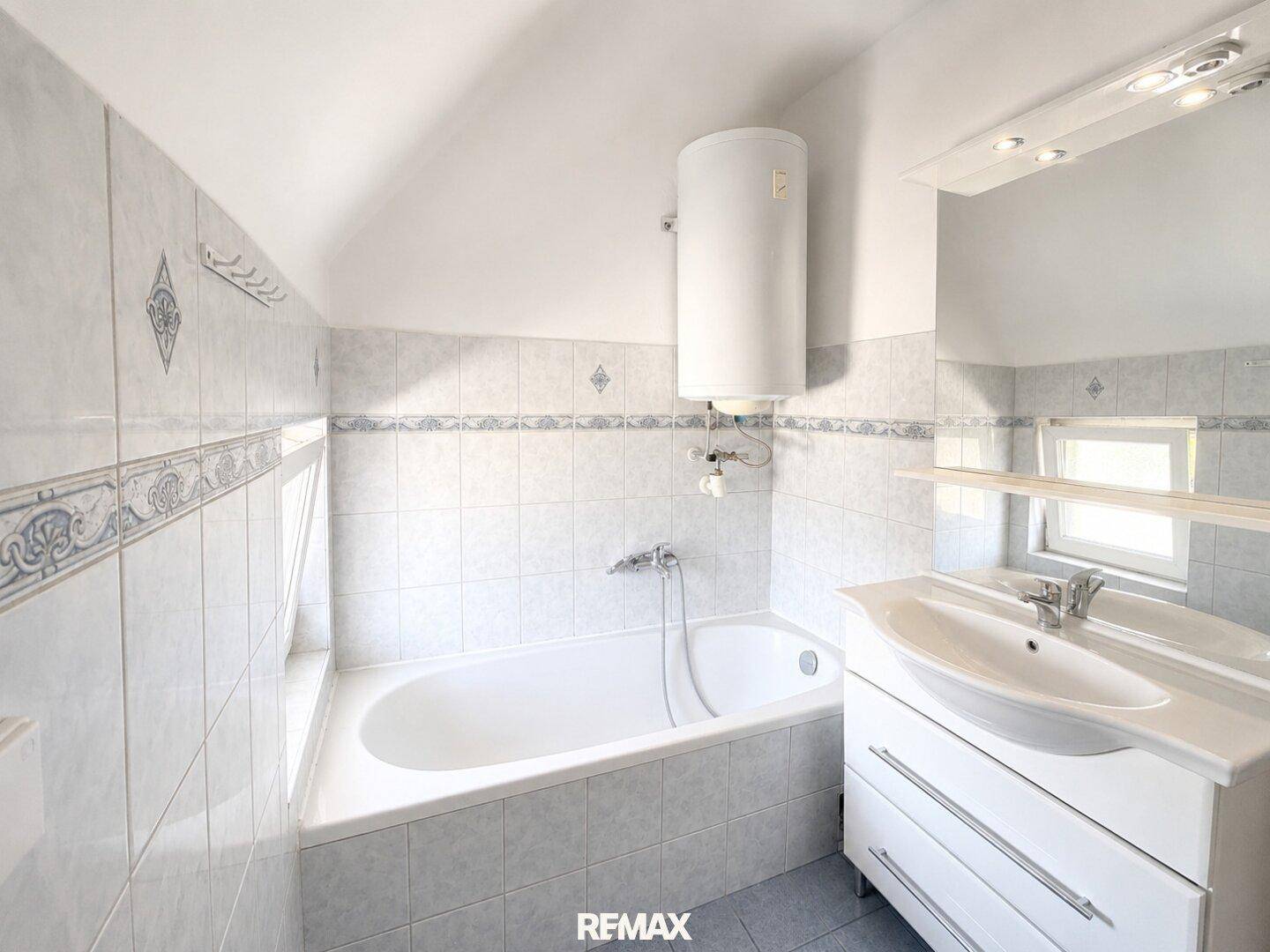Helles Badezimmer mit Badewanne, Waschbecken und Fliesen in hellem Design.