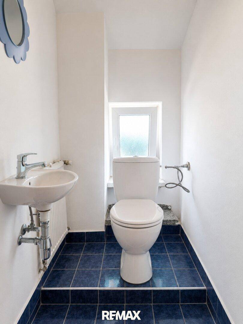 Kleines Gäste-WC mit blauen Fliesen, Toilette und Handwaschbecken.