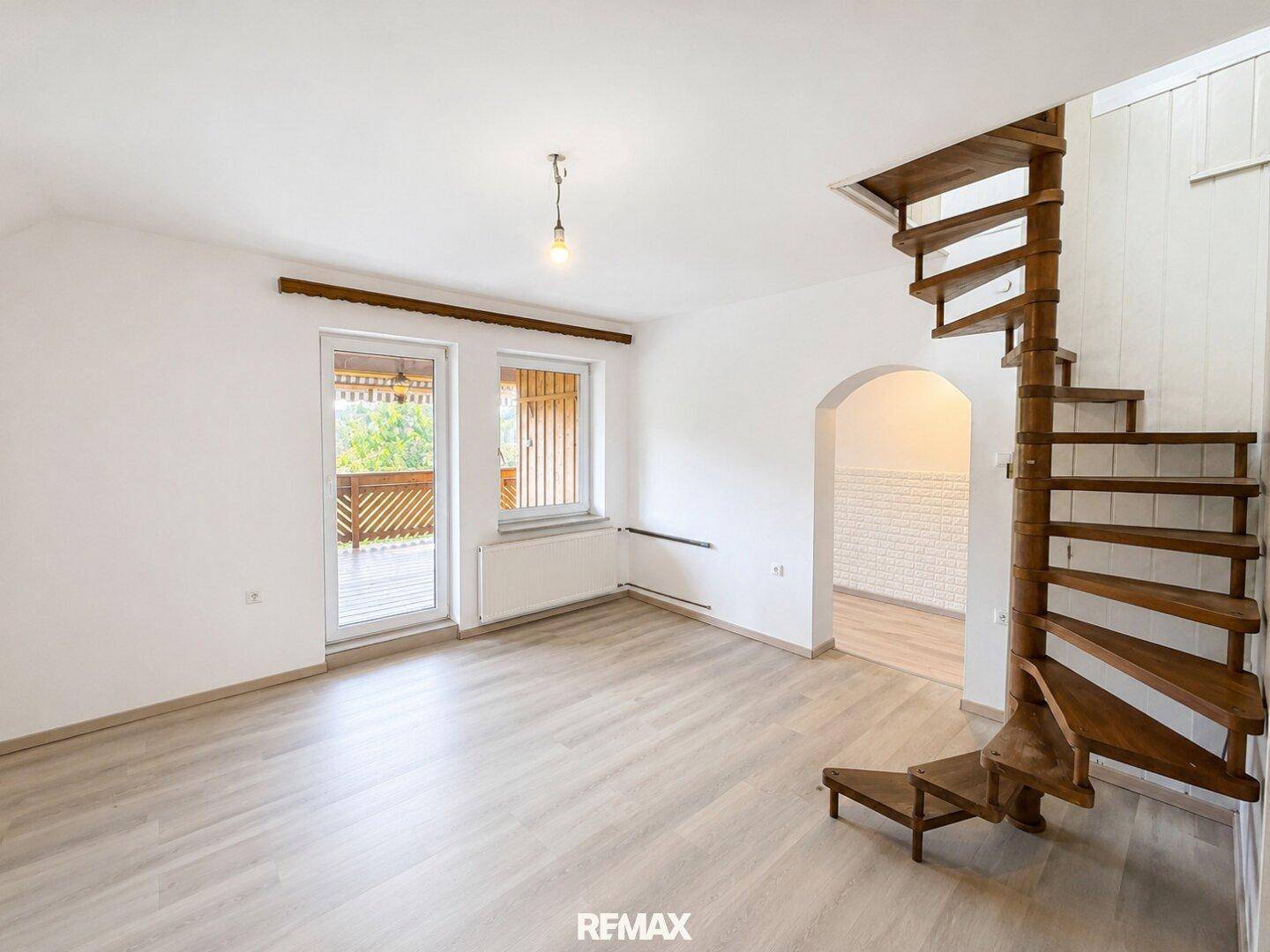 Heller Raum mit Laminatboden, Wendeltreppe und Zugang zu einem Balkon.
