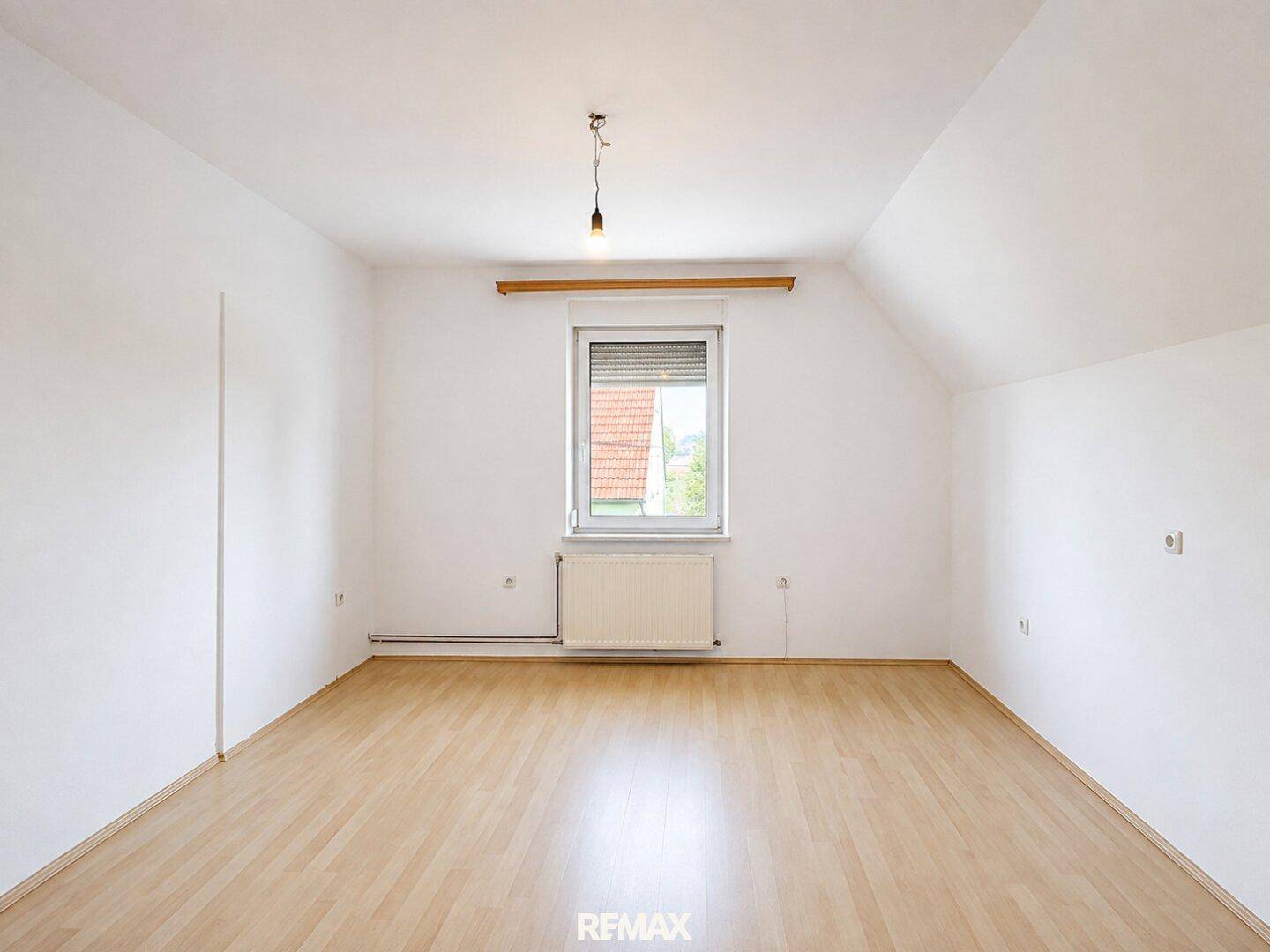 Geräumiges, leeres Schlafzimmer mit Laminatboden und Fenster mit Rollladen.