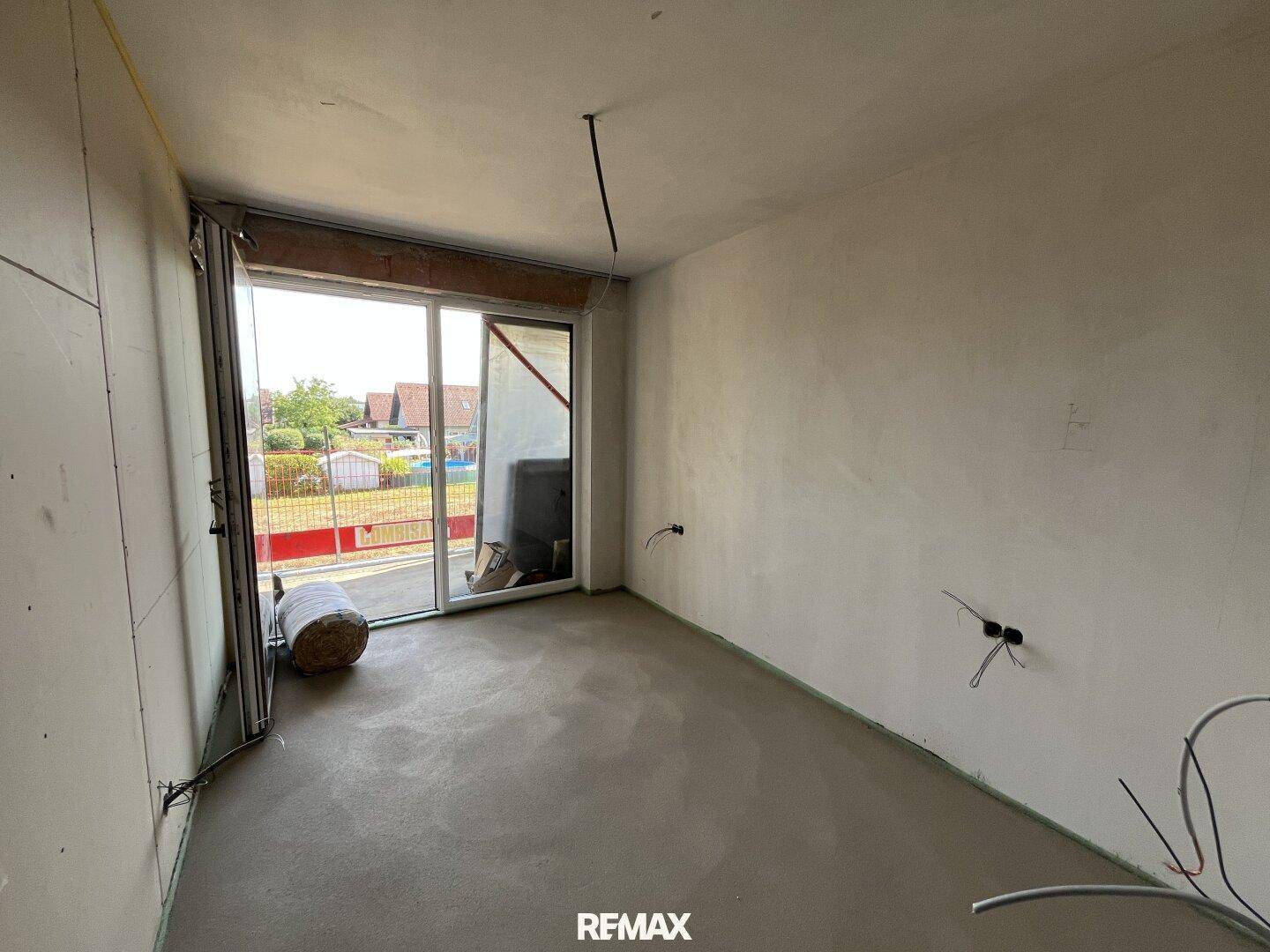 Innenraum im Rohbau mit Betonboden und großer Schiebetür zum Außenbereich.