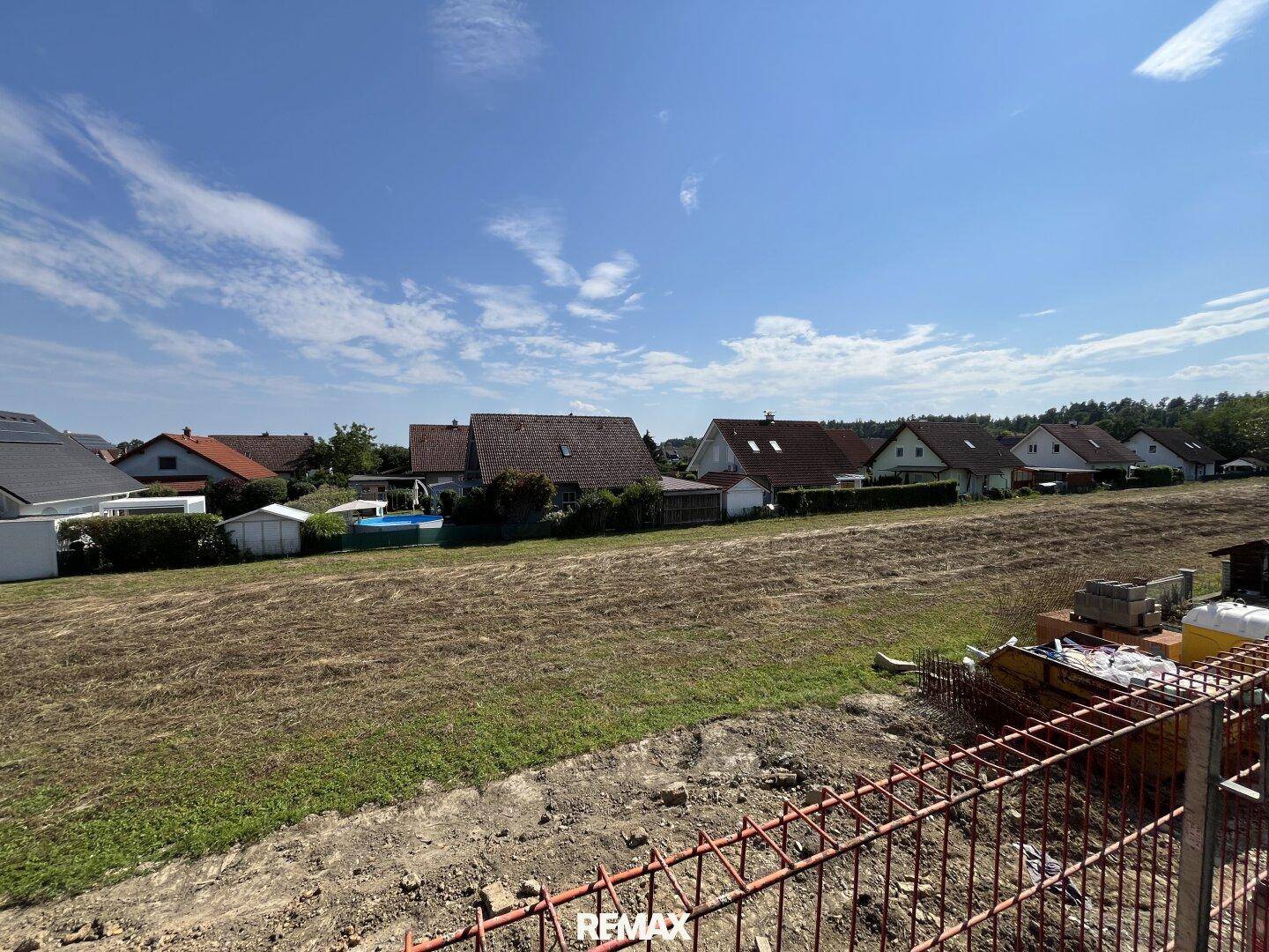 Blick über ein Baugrundstück mit angrenzenden Wohnhäusern unter blauem Himmel.