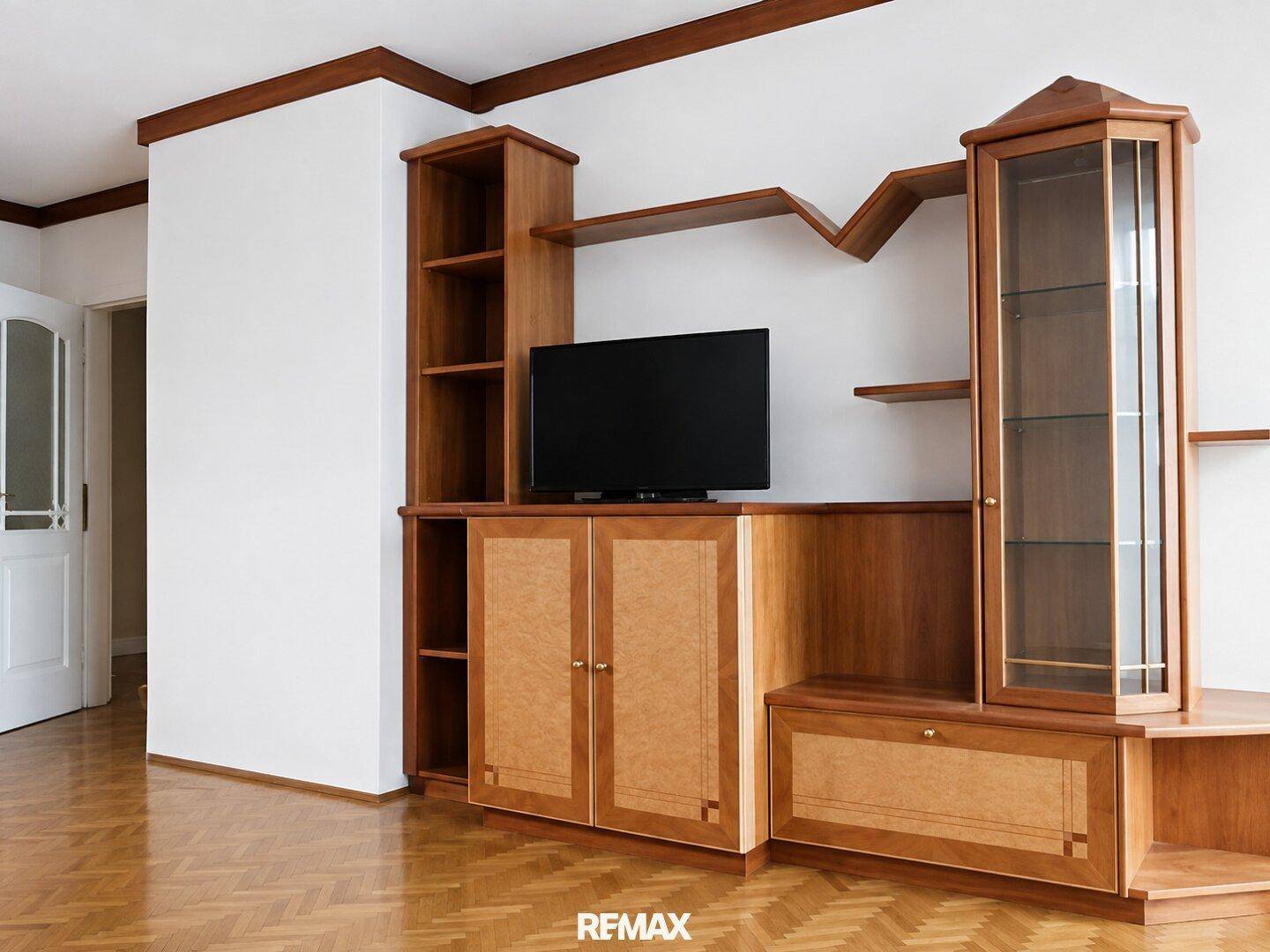 Wohnzimmer mit maßgefertigter Holzschrankwand, Fernseher und Parkettboden.