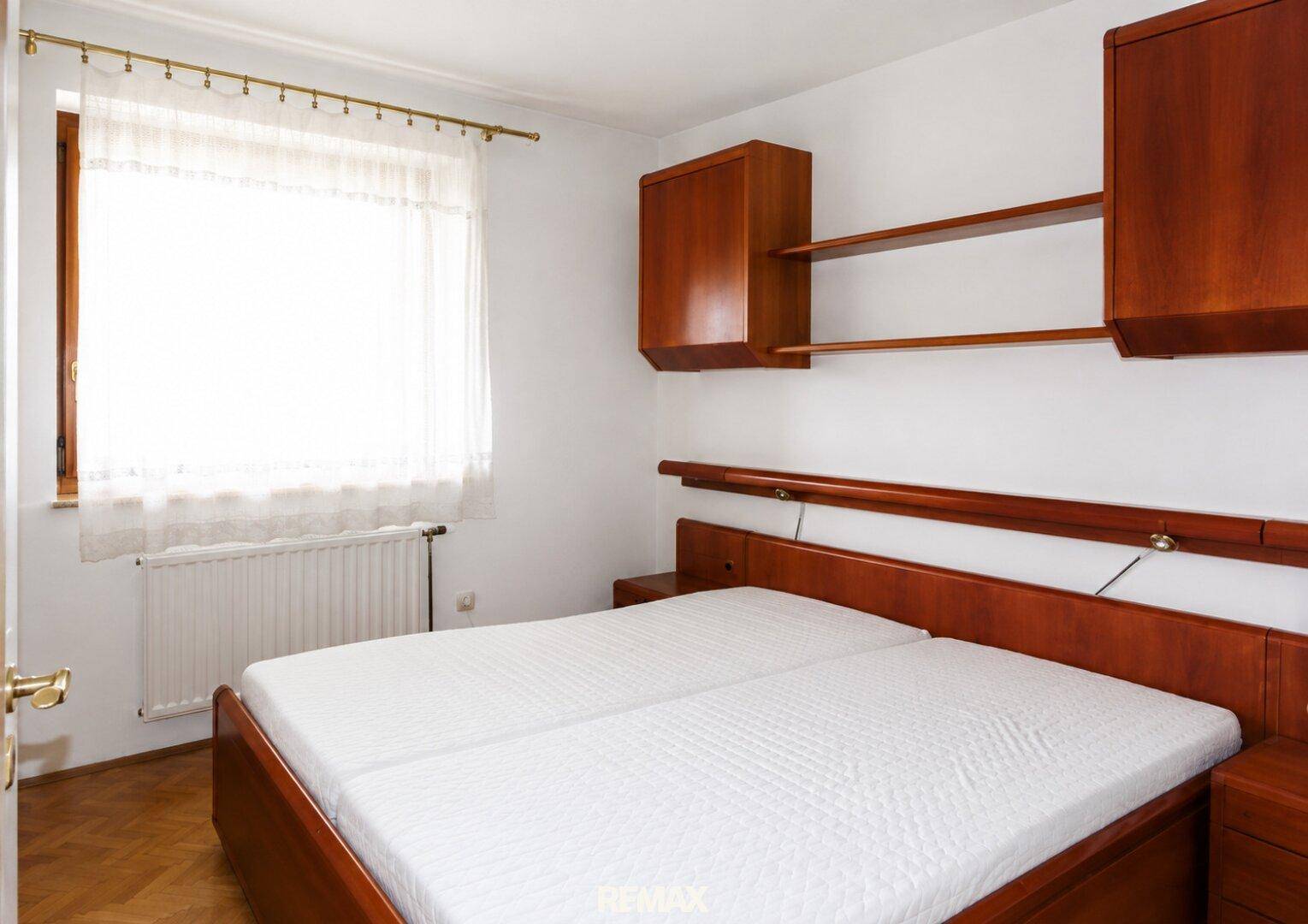 Schlafzimmer mit Doppelbett, Holzmöbeln und Fenster, das viel Tageslicht hereinlässt.