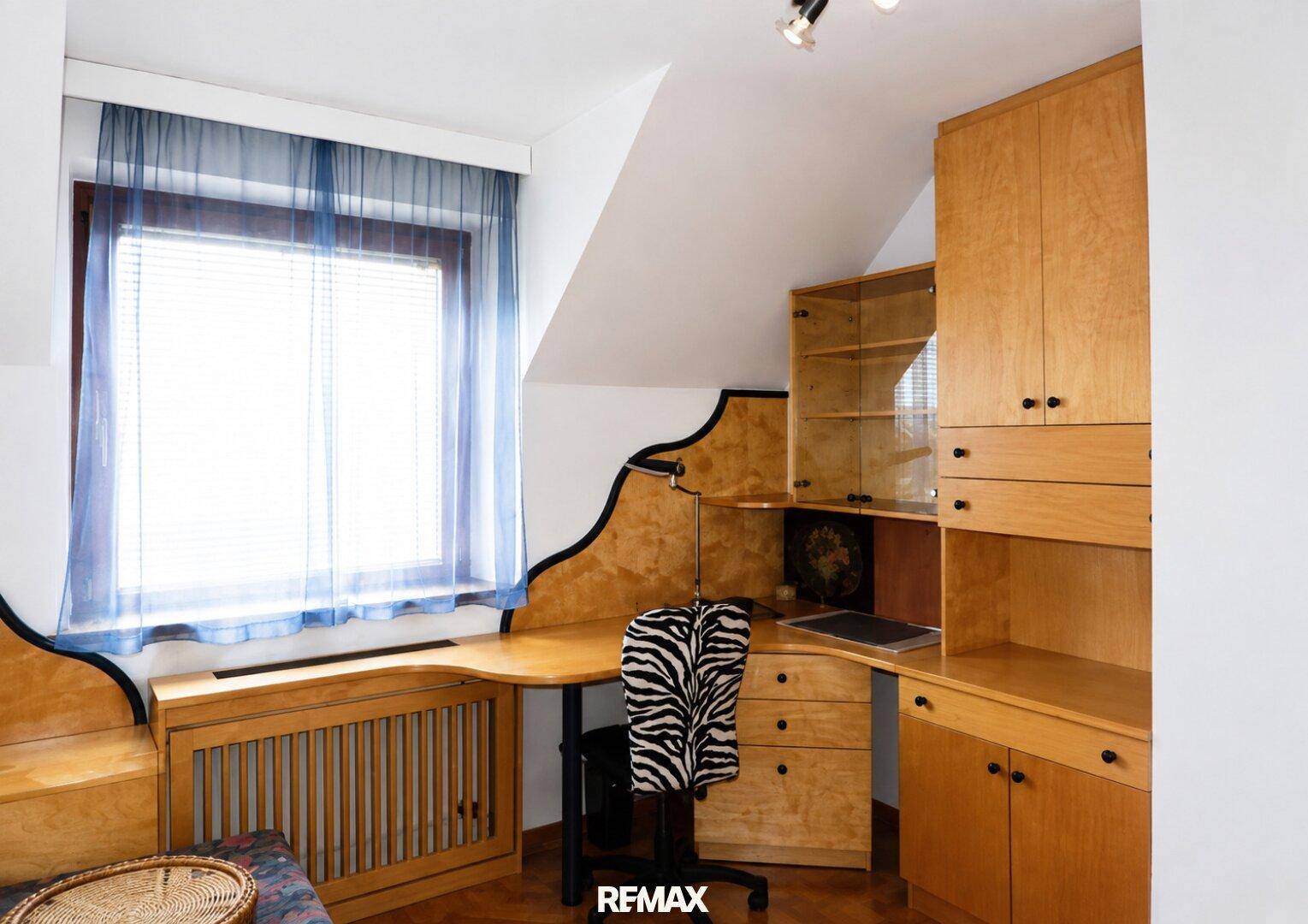 Arbeitszimmer mit maßgefertigtem Schreibtisch, Holzschränken und Dachschräge.