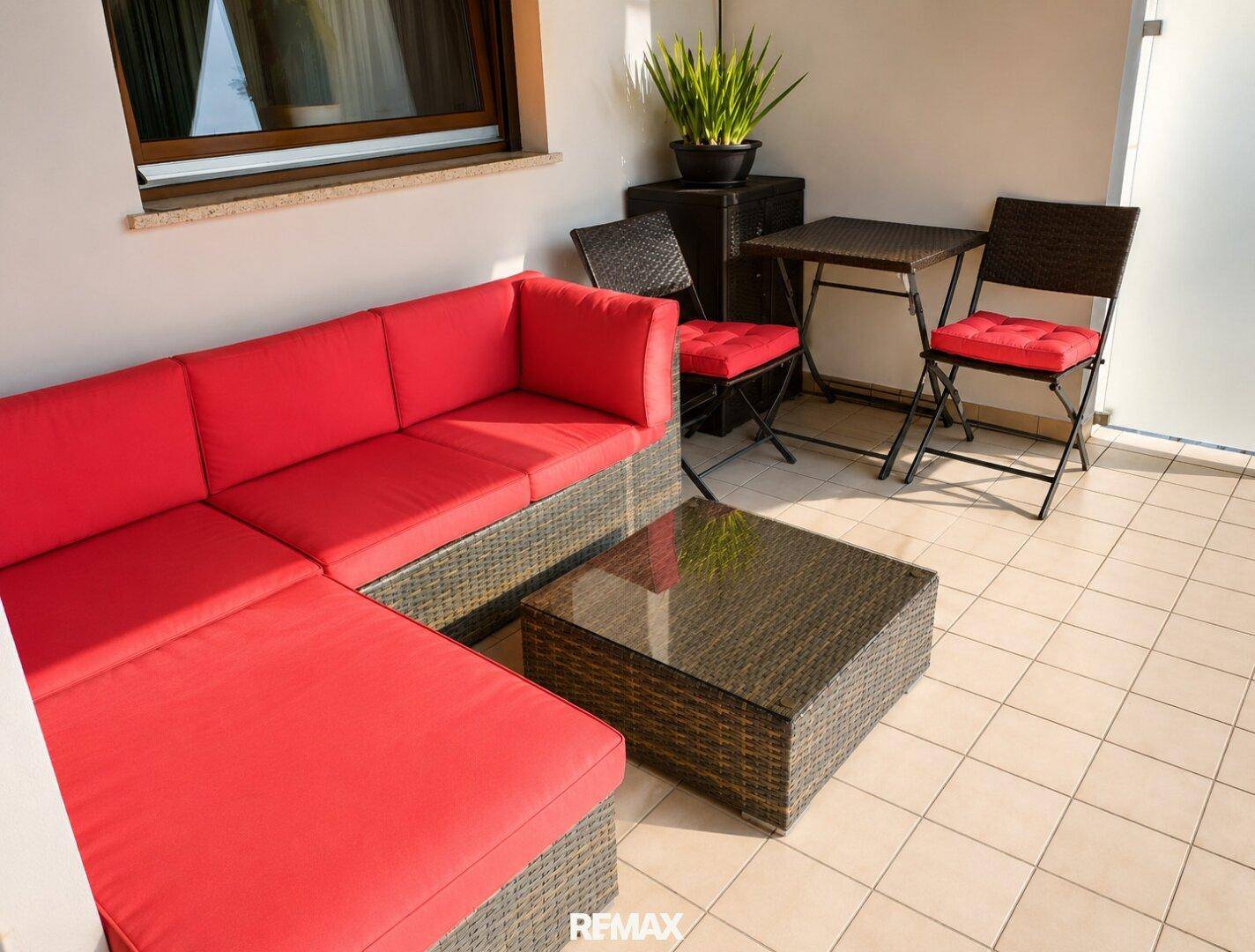 Gemütliche Terrasse mit Rattanmöbeln, roten Kissen und Fliesenboden.