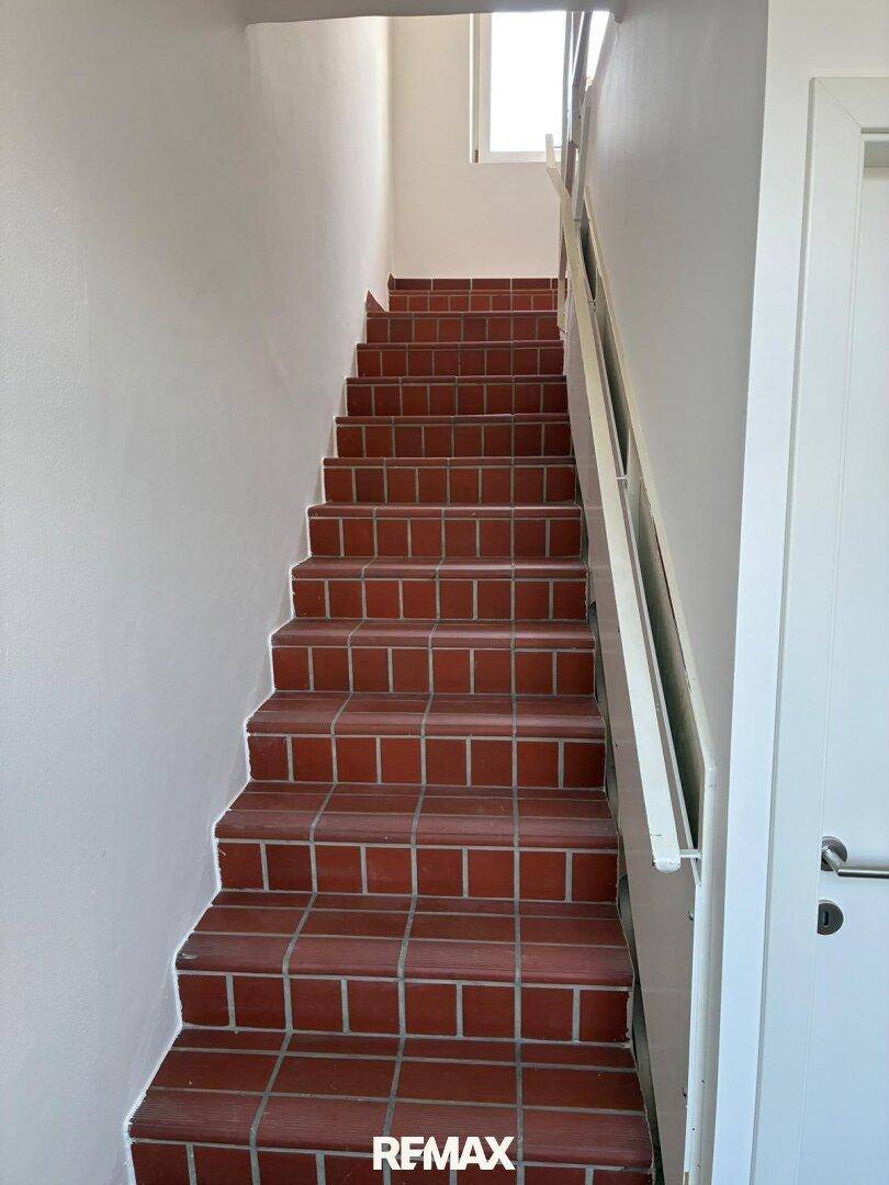Treppenhaus mit Terrakottafliesen und weiß gestrichenen Wänden, das nach oben führt.