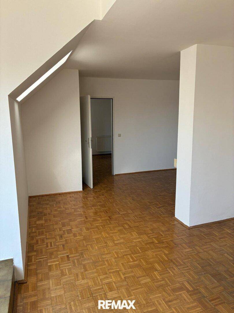 Geräumiger Raum mit Parkettboden und Dachschräge, der durch eine offene Tür zugänglich ist.