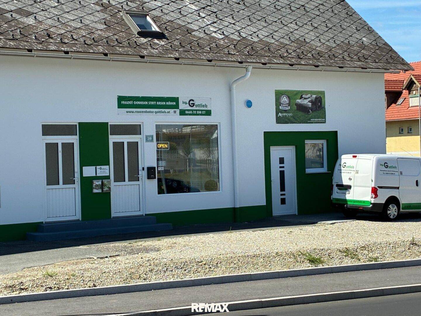 Ansicht eines Geschäftsgebäudes mit weißer Fassade, grünen Details und einem geparkten Fahrzeug.