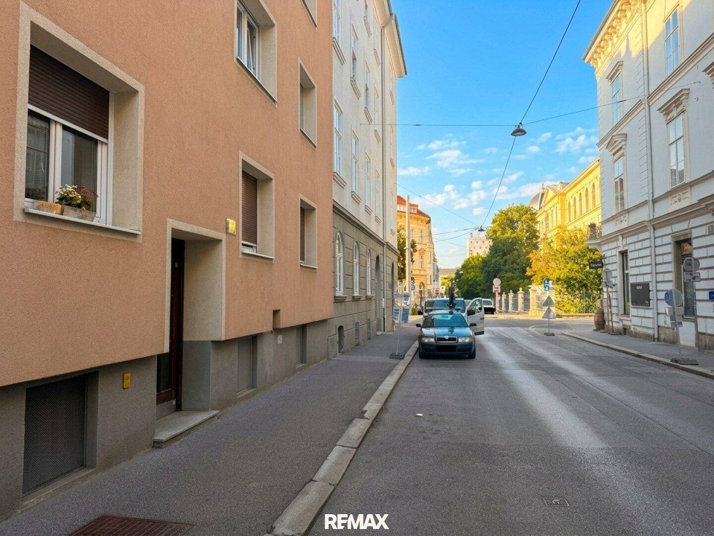 Ruhige Wohnstraße mit gepflegten Gebäudefassaden und parkenden Autos unter blauem Himmel.