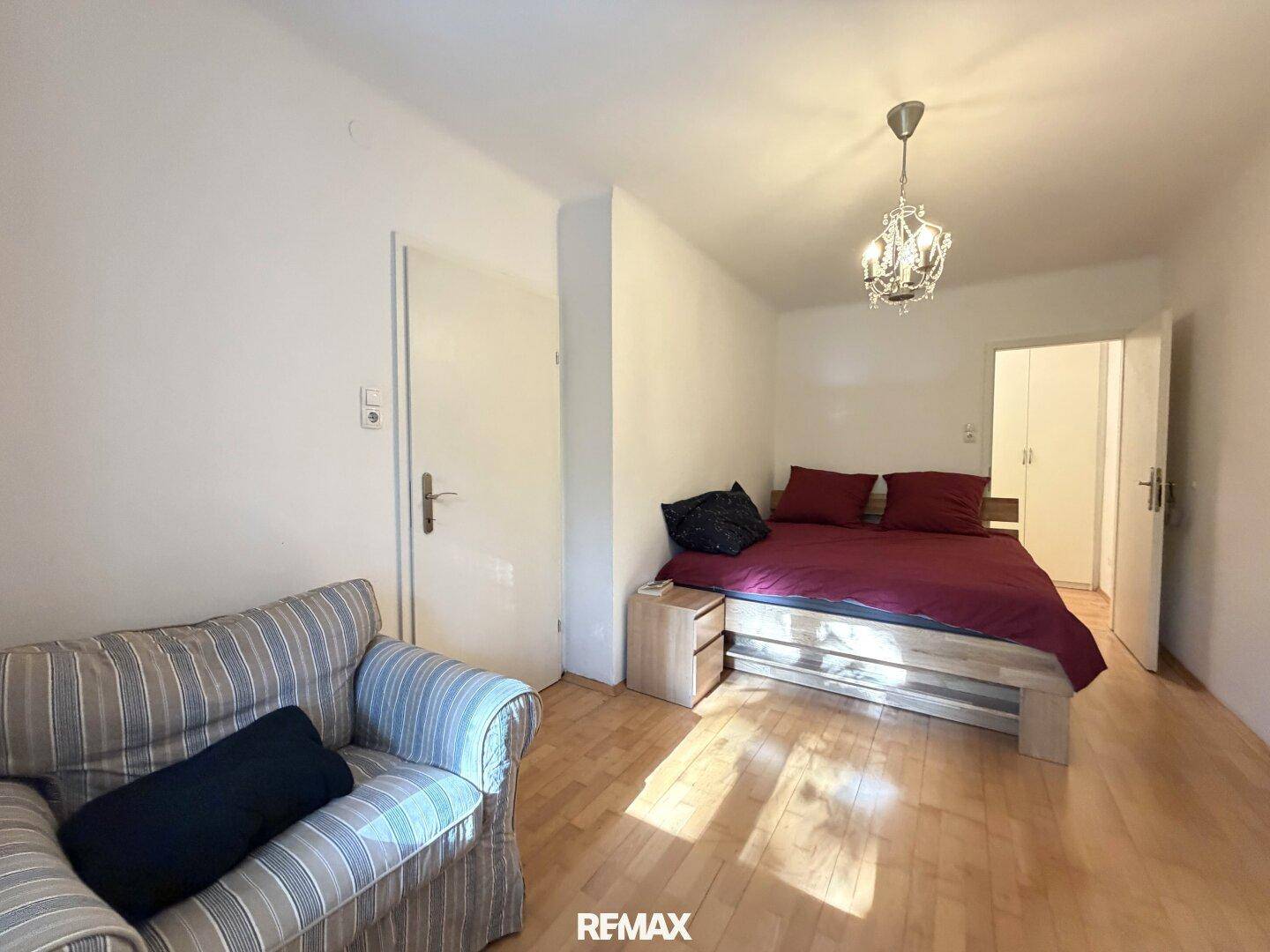 Schlafzimmer mit Holzboden, einem Bett und einem kleinen Sofa, das eine gemütliche Atmosphäre schafft.