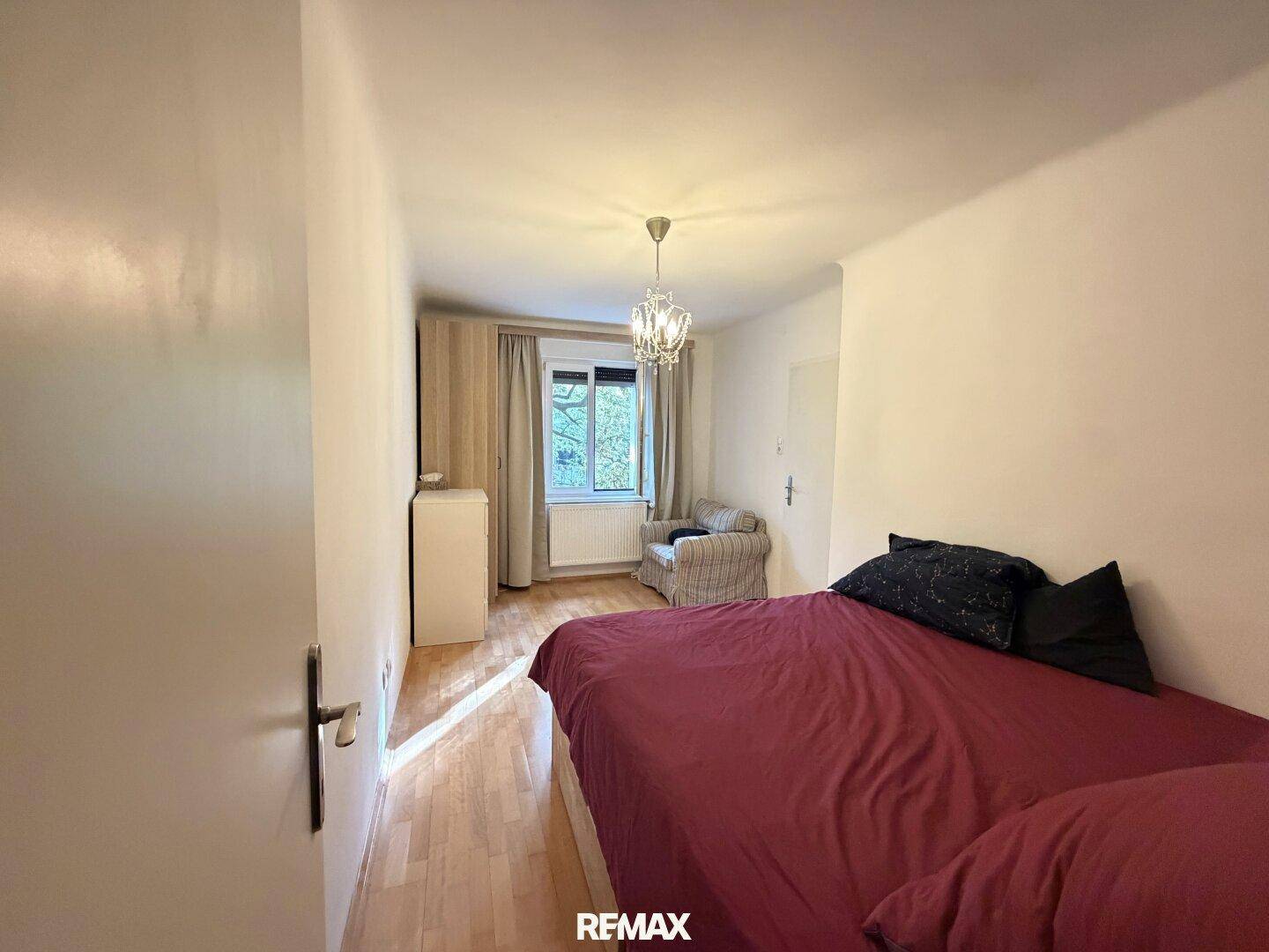 Schlafzimmer mit Holzboden, einem Bett und einem Fenster, das viel Tageslicht hereinlässt.