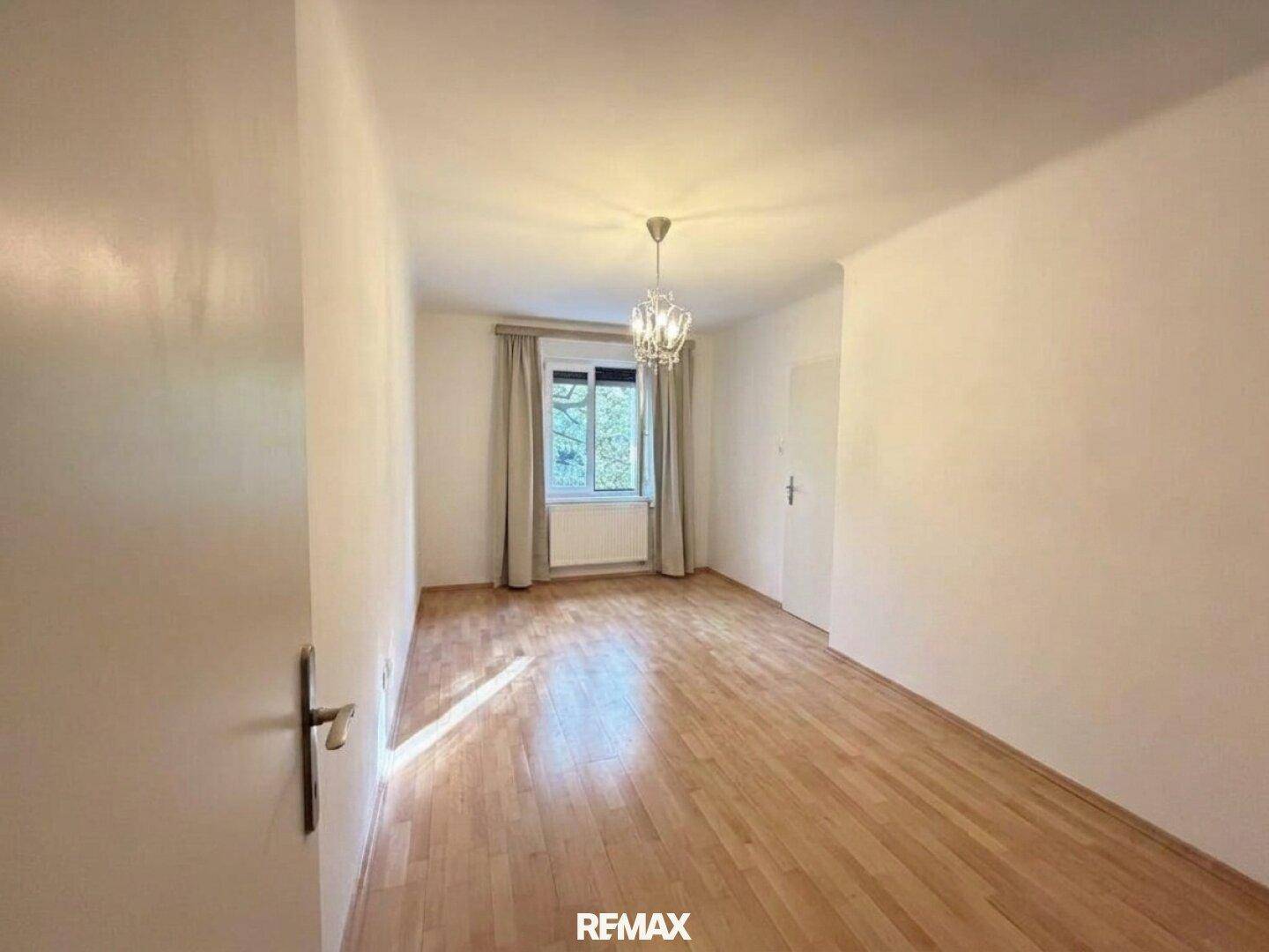 Unmöbliertes Schlafzimmer mit hellem Parkettboden und einem Fenster, das den Raum erhellt.