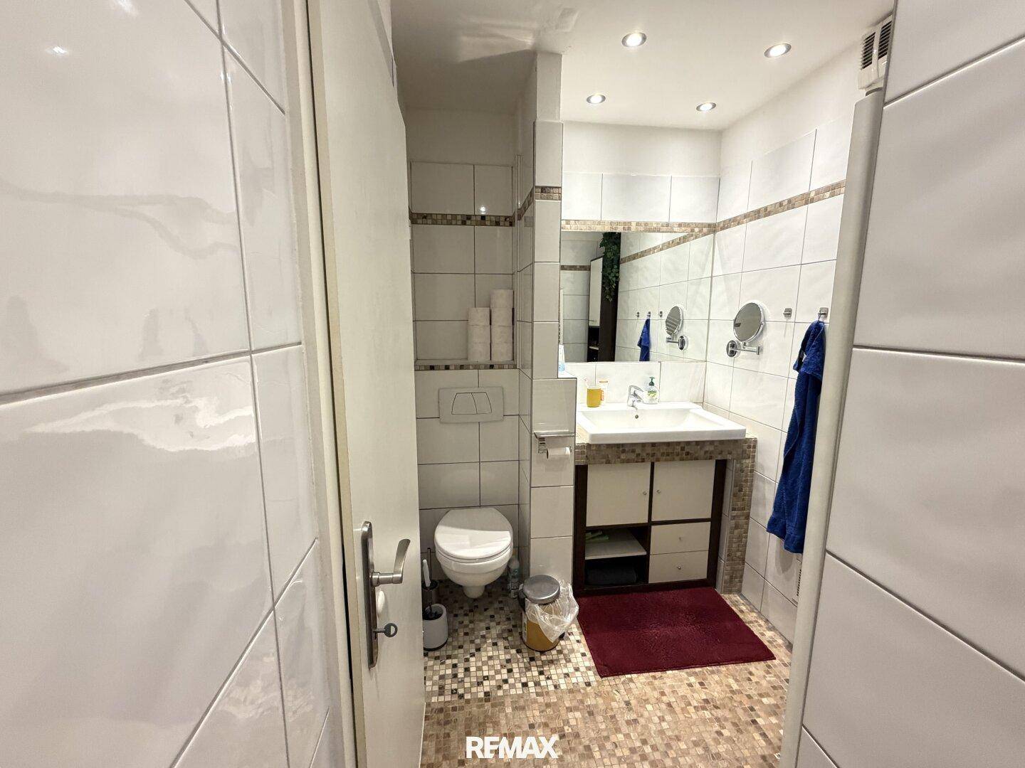 Gefliestes Badezimmer mit WC, Waschbecken und einem Spiegel, der den Raum optisch vergrößert.