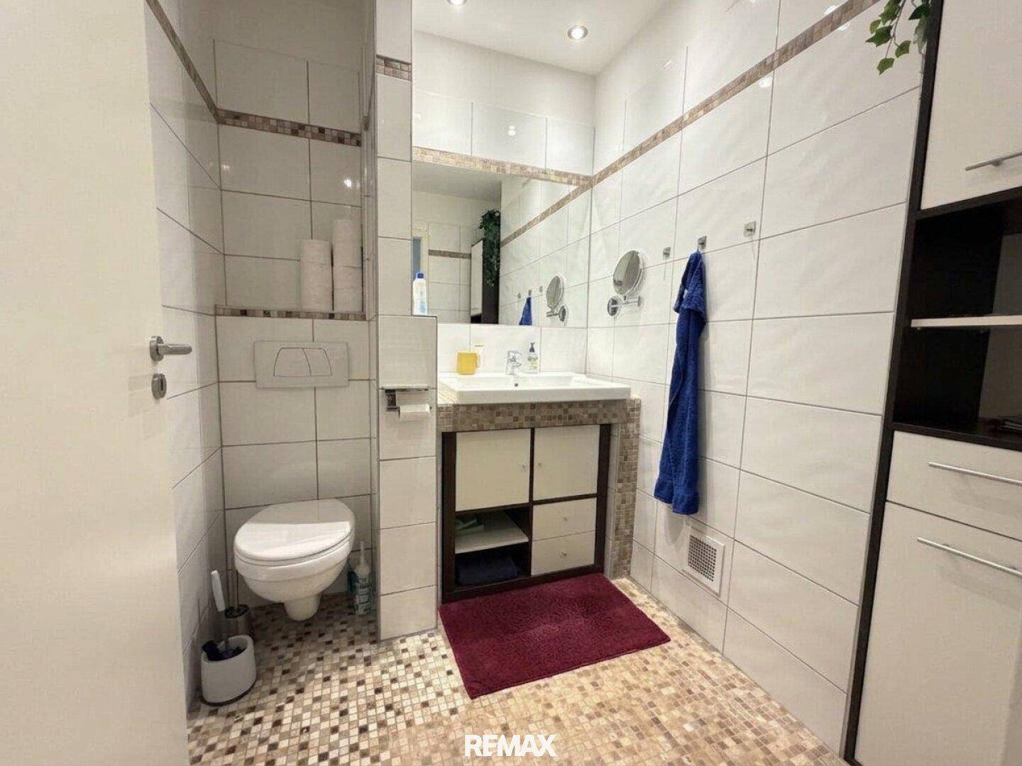 Modern gefliestes Badezimmer mit WC, Waschbecken und einem dekorativen Mosaikboden.
