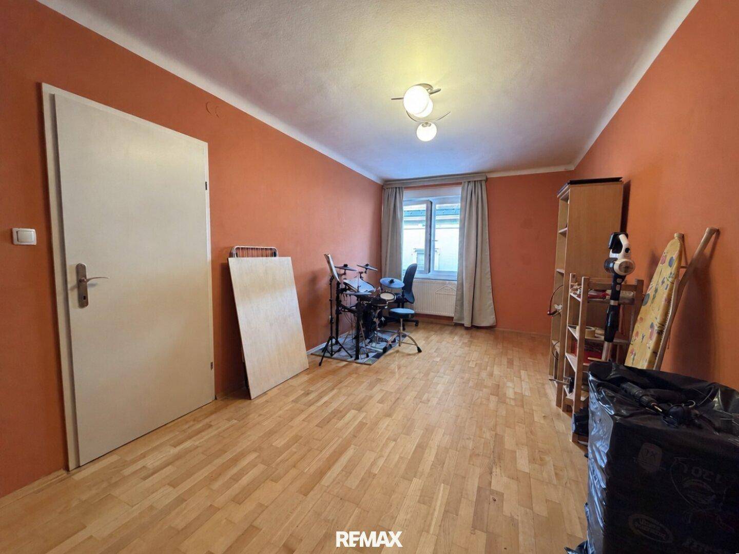 Vielseitiger Raum mit orangefarbenen Wänden und Parkettboden, derzeit als Musikzimmer genutzt.