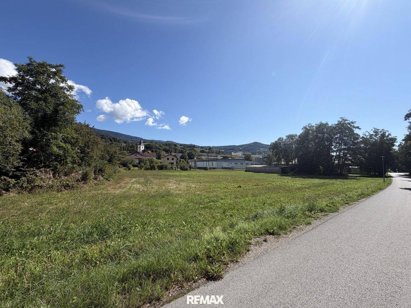 Offenes Feld mit weitem Blick auf die grüne Umgebung, Berge und einen klaren blauen Himmel an einem sonnigen Tag.