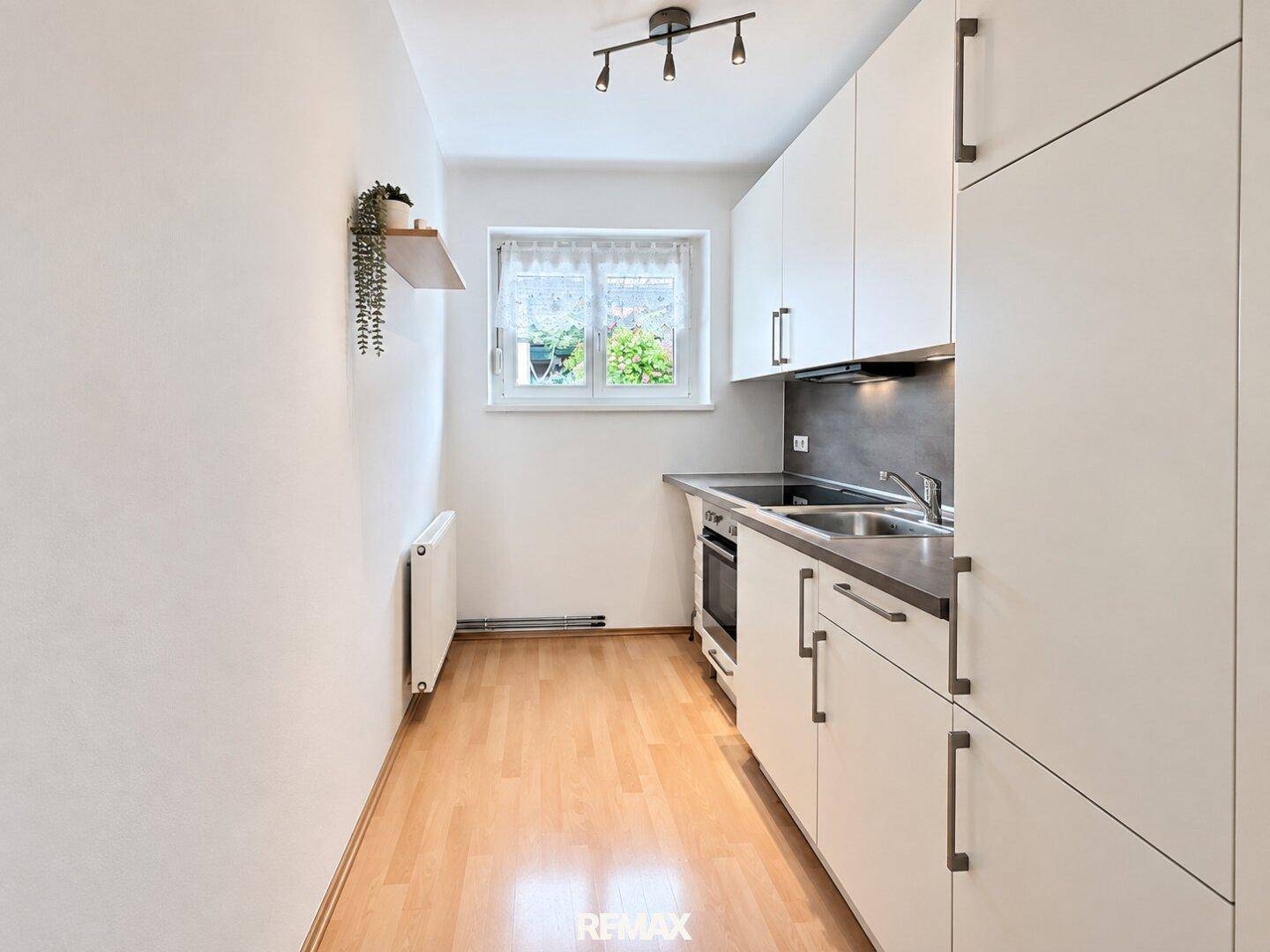 Funktionale Küchenzeile mit weißen Schränken, Kochfeld und Fenster, ideal für kleine Haushalte.