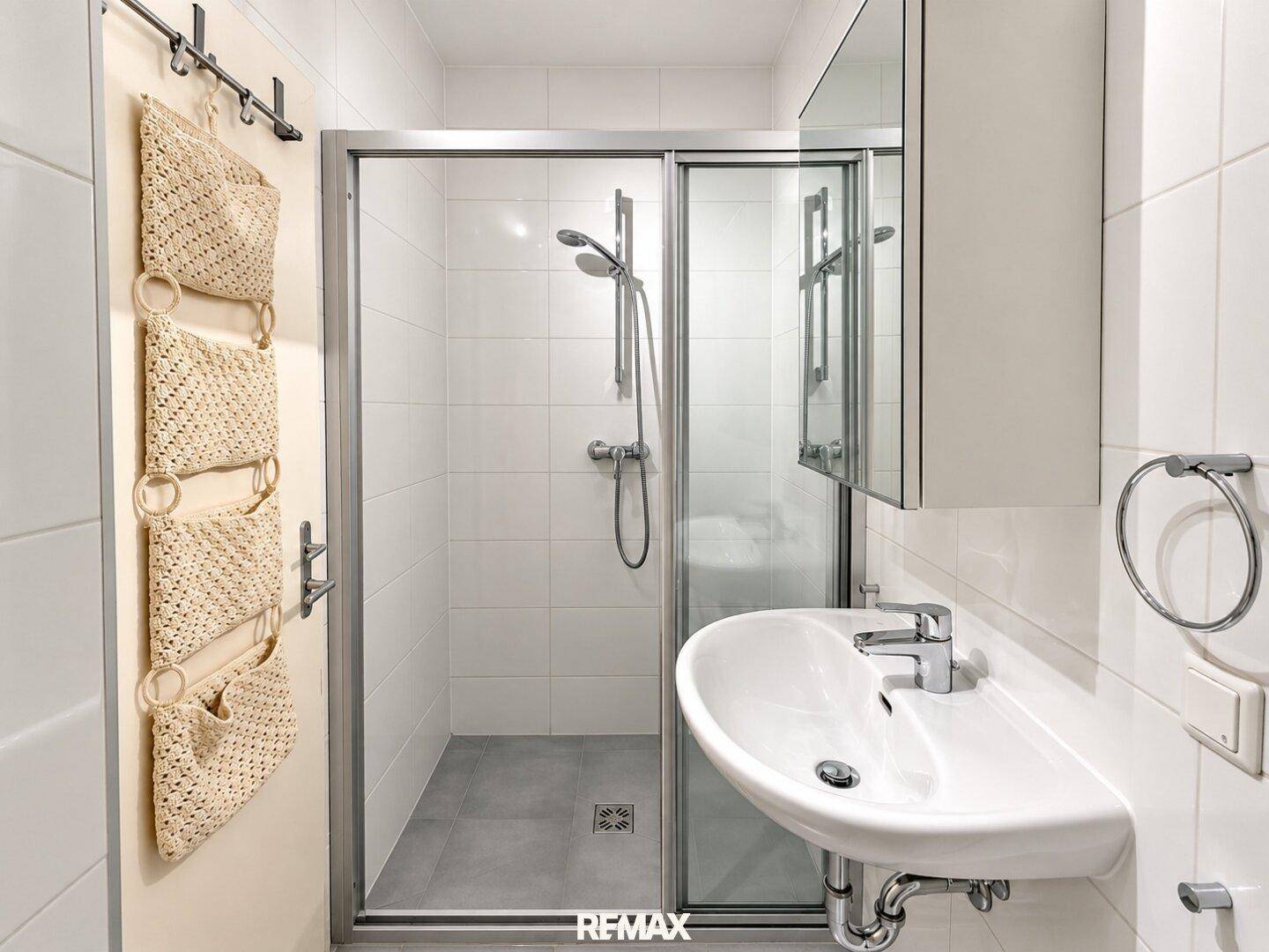 Modernes Badezimmer mit Duschkabine und Waschbecken, hell gefliest.
