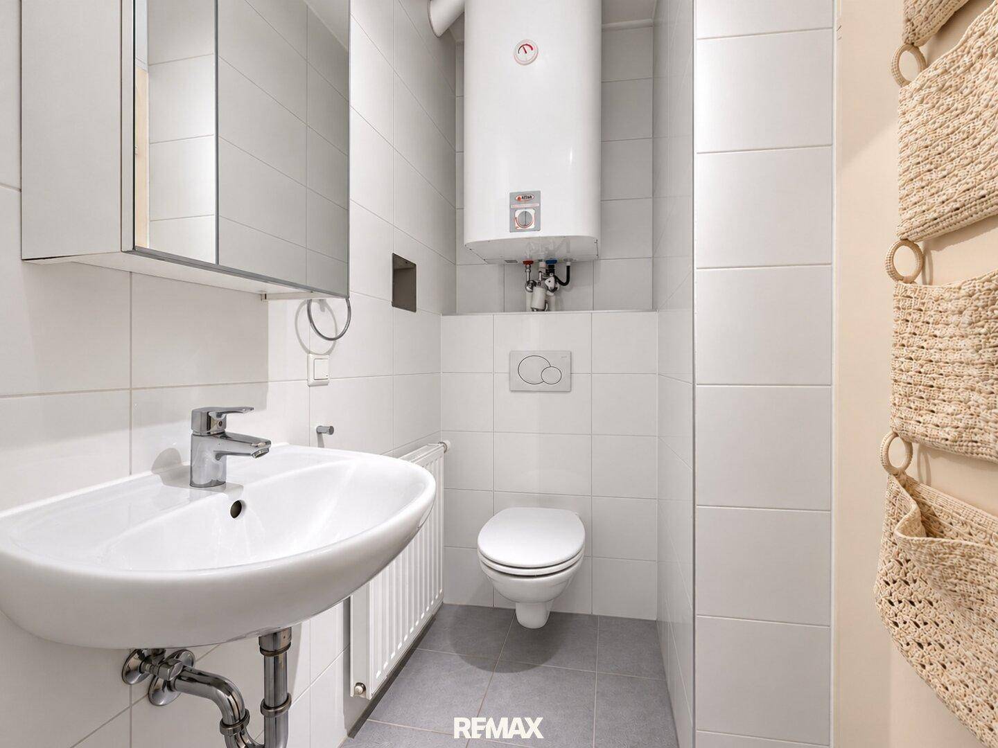 Kompaktes Badezimmer mit wandhängendem WC, Waschbecken und Warmwasserboiler.