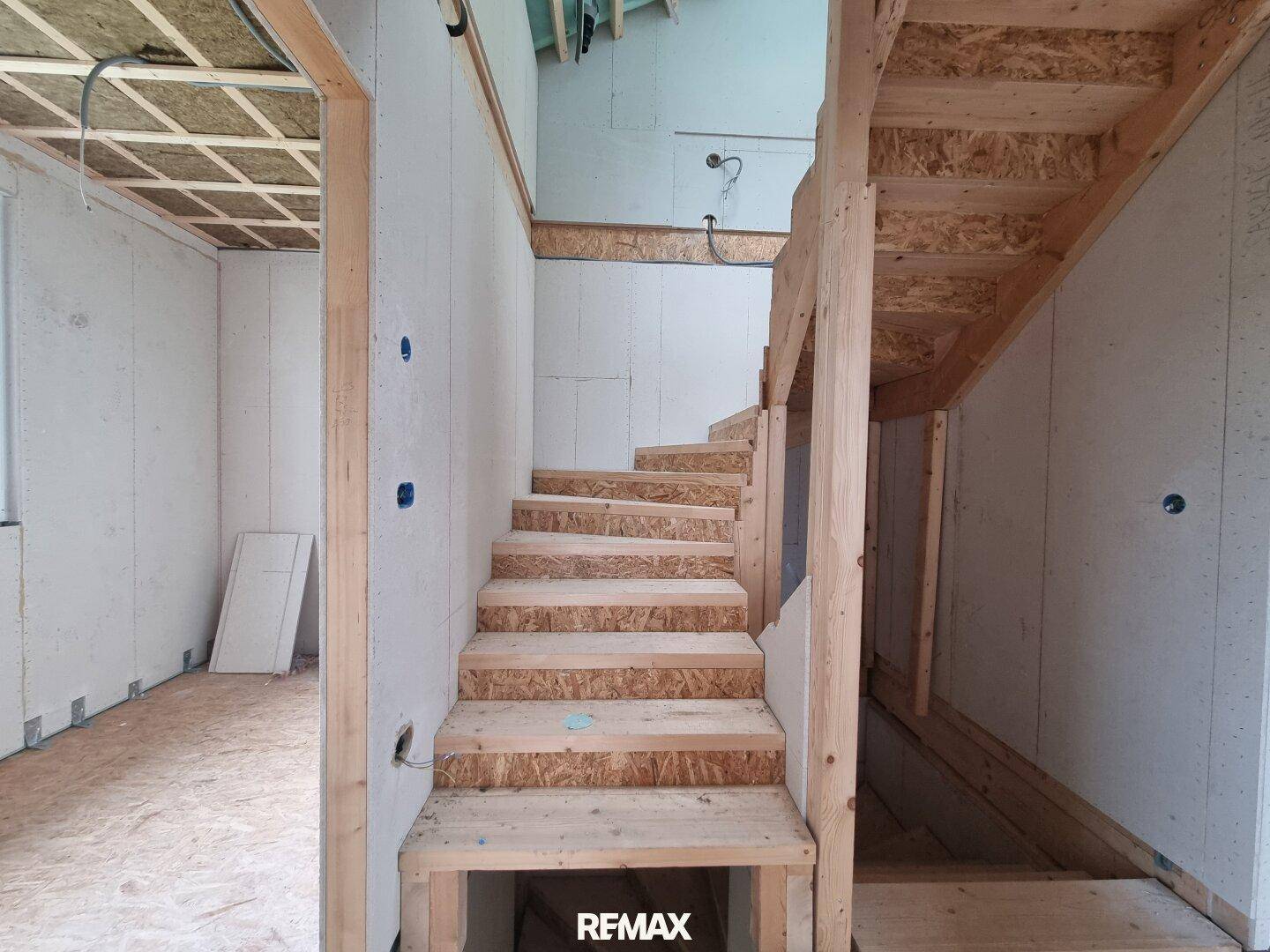 Holztreppe im Rohbau, die in das obere Stockwerk führt, mit sichtbaren Holzkonstruktionen.