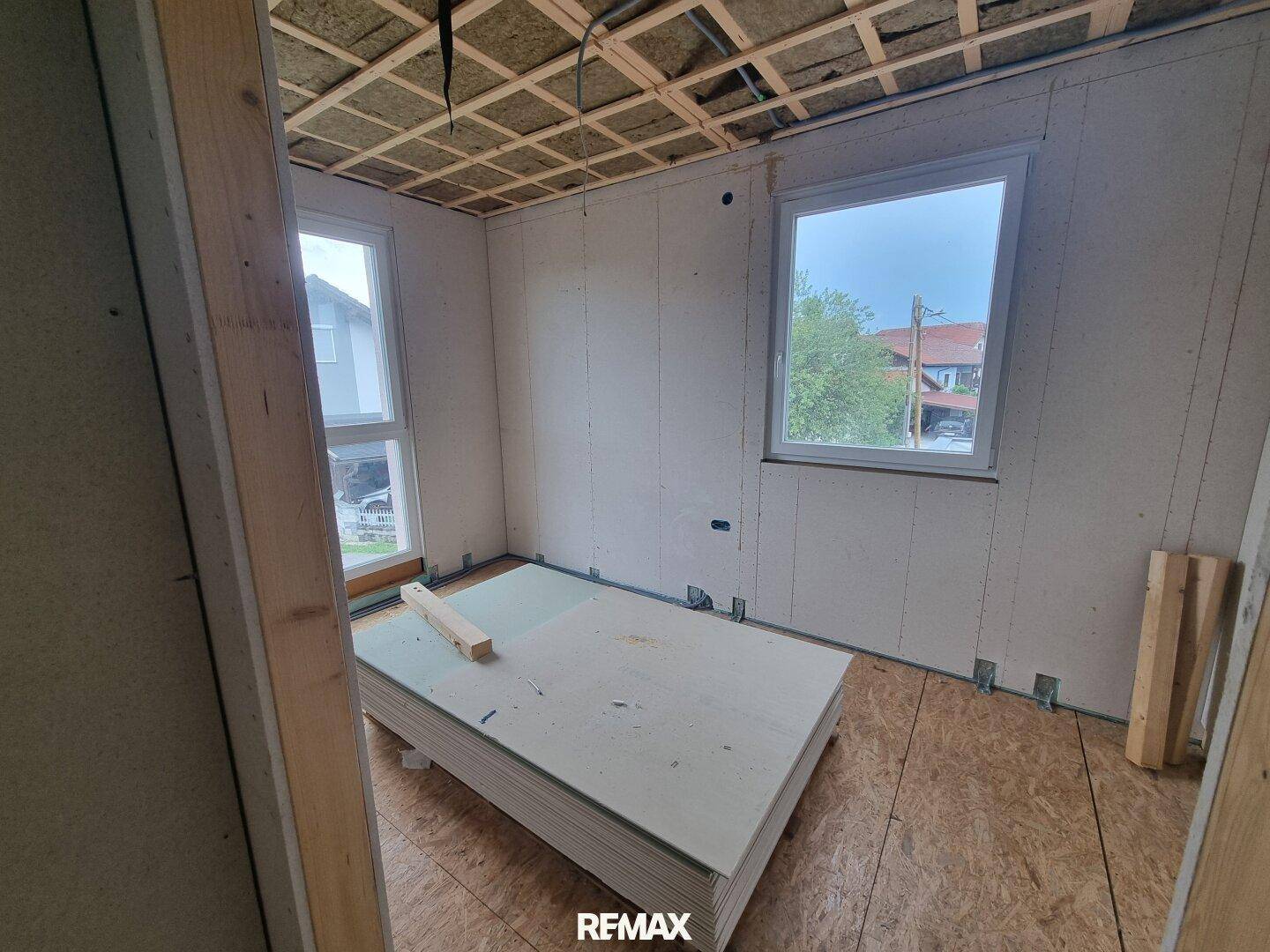 Rohbauzimmer mit zwei Fenstern und Holzspanplattenboden, bereit für weitere Ausbauarbeiten.