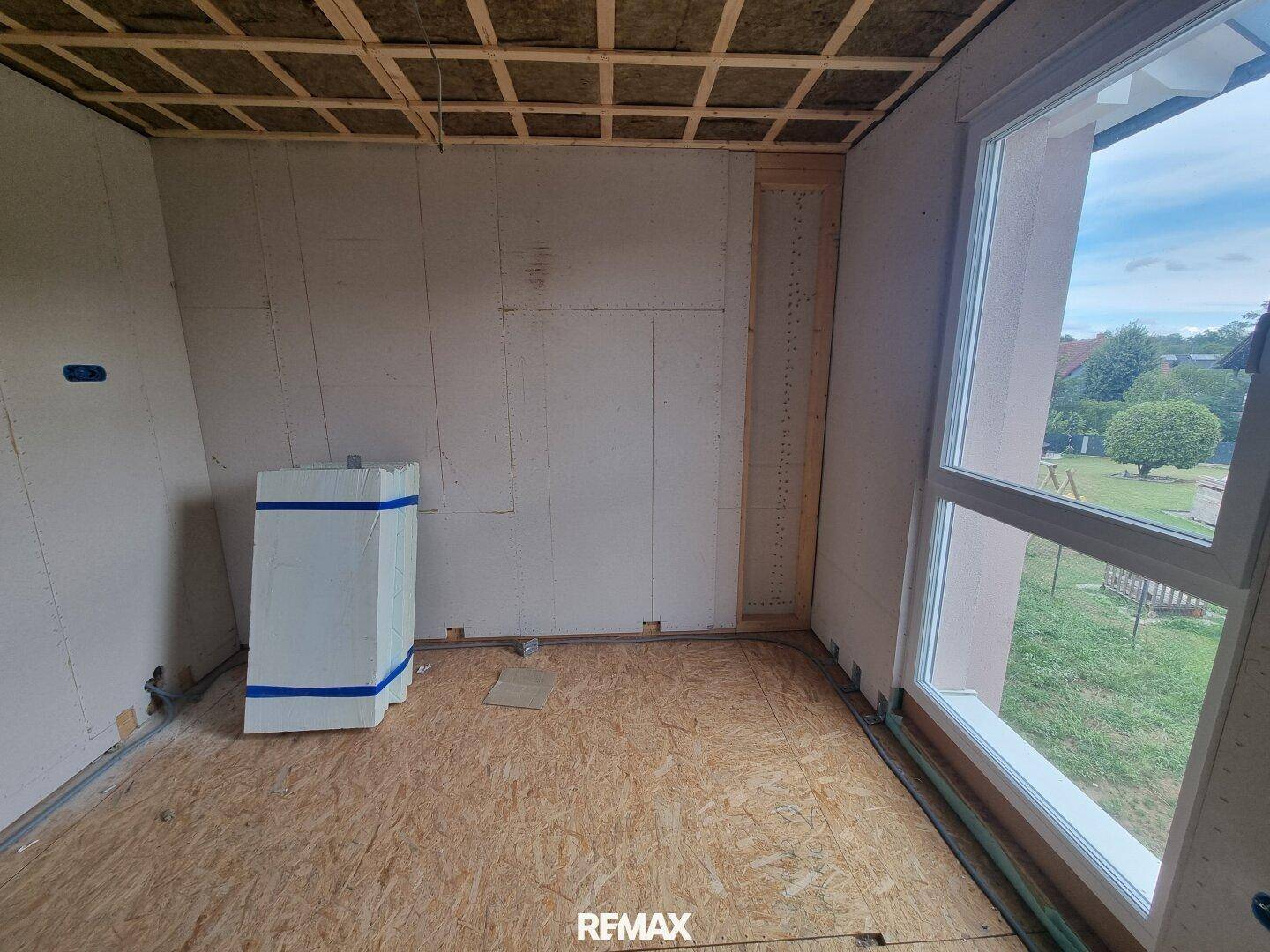 Rohbauzimmer mit großer Fensterfront und Blick auf die Umgebung, mit Dämmmaterial an der Decke.