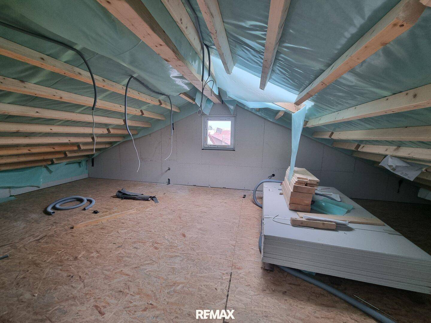 Dachgeschoss im Rohbau mit sichtbaren Dachbalken und einem Dachfenster, bereit für den Ausbau.