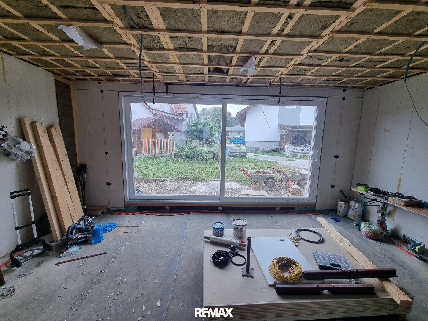 Innenraum im Rohbau mit großer Fensterfront und Blick ins Grüne, bereit für den Ausbau.