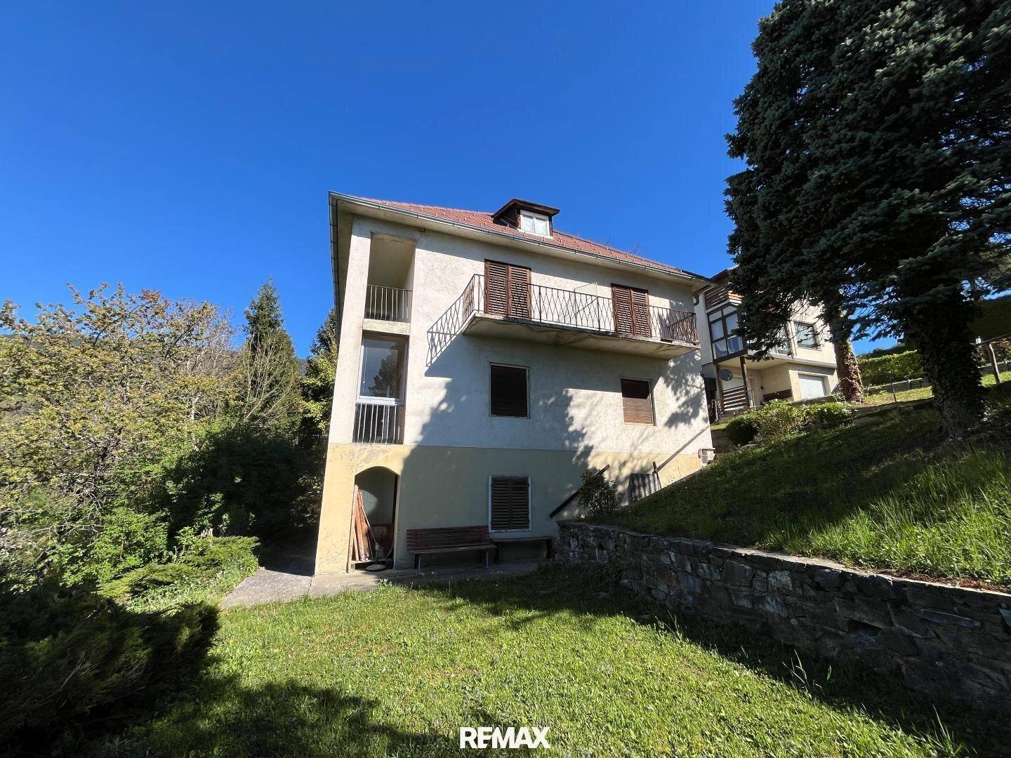 Ansicht des Hauses von der Seite mit Balkon und Treppe, umgeben von Bäumen.
