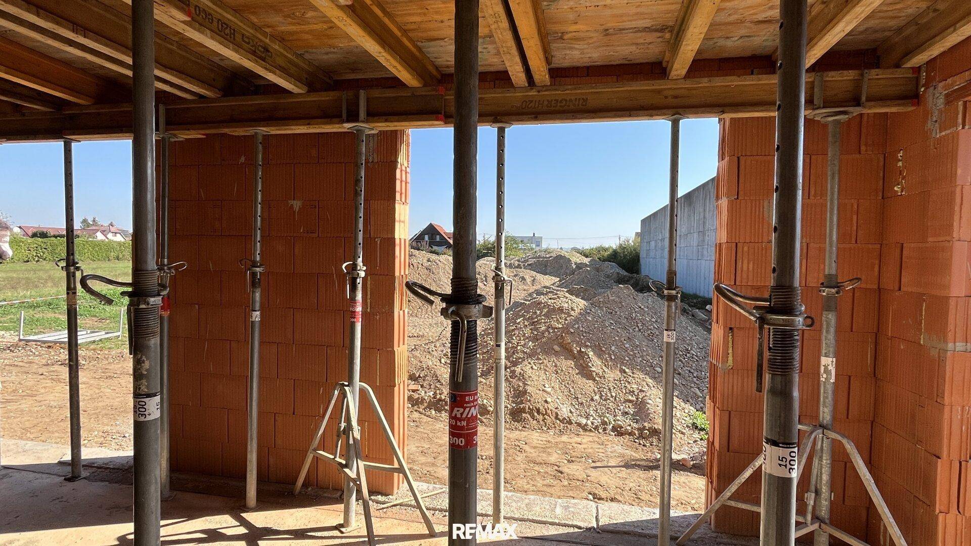 Blick aus dem Rohbau auf die Baustelle und die Umgebung mit Erdhügeln.