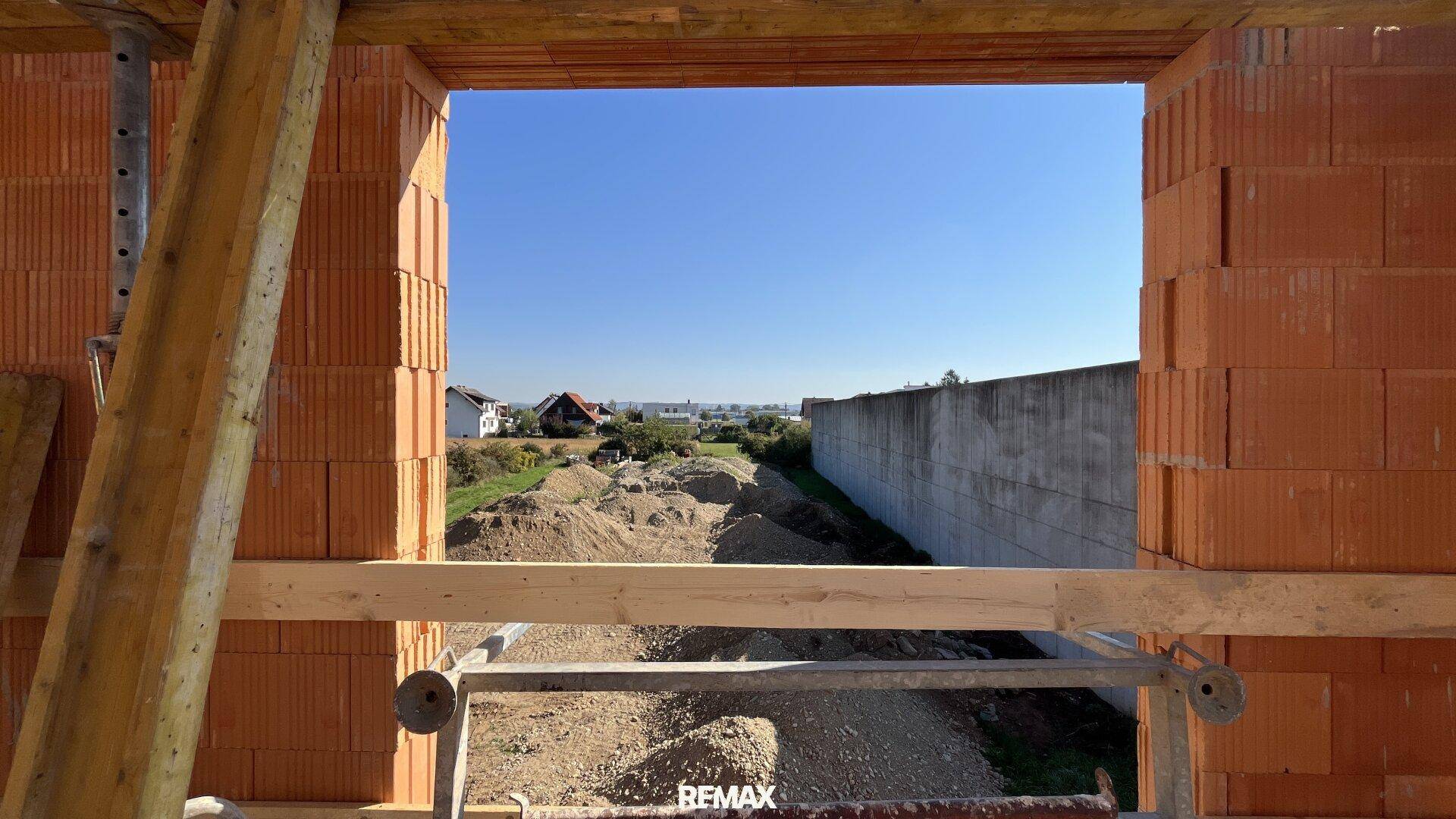 Blick durch eine Fensteröffnung im Rohbau auf die ländliche Umgebung und den Horizont.