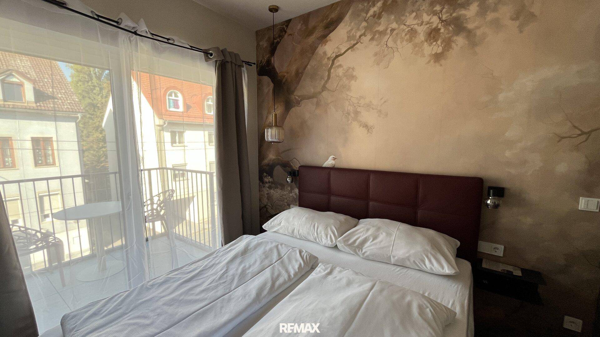 Gemütliches Schlafzimmer mit Doppelbett, Balkonzugang und einer malerischen Wandtapete.