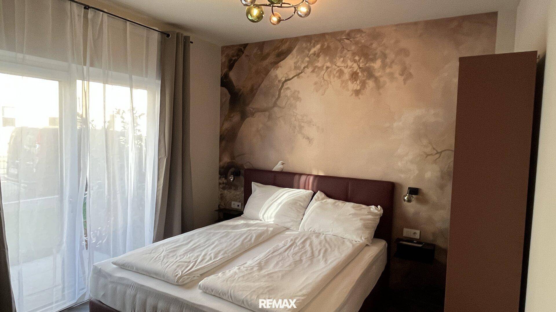 Schlafzimmer mit Doppelbett, Baum-Wandtapete und Zugang zu einer Terrasse.