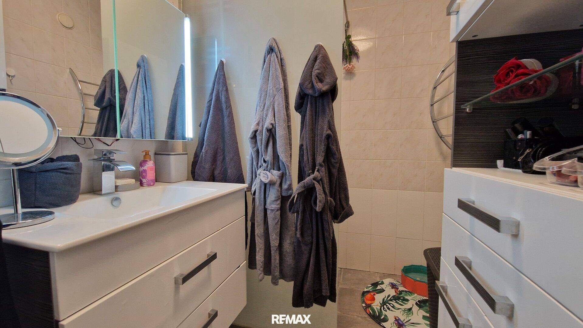 Badezimmer mit Waschtisch, Spiegel und hellen Fliesen an den Wänden.