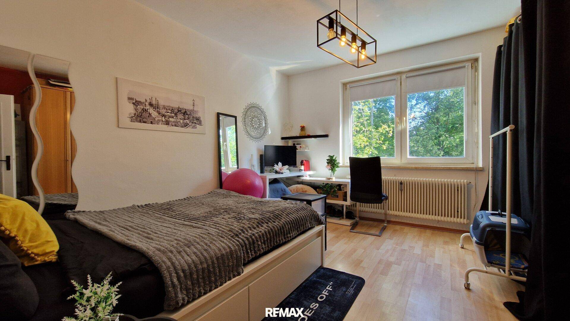 Schlafzimmer mit Bett, Schreibtisch und Fenster mit Blick ins Grüne.